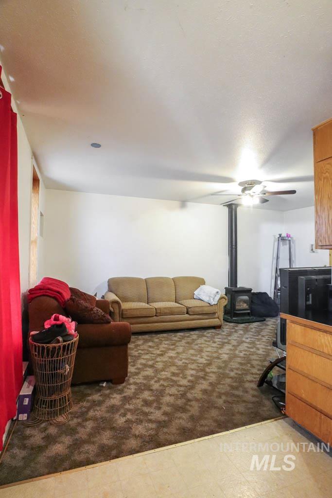 Living room with a wood stove, a ceiling fan, and light flooring