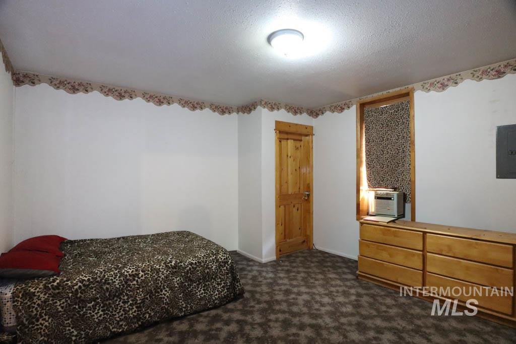 Bedroom with dark colored carpet, a textured ceiling, electric panel, and cooling unit