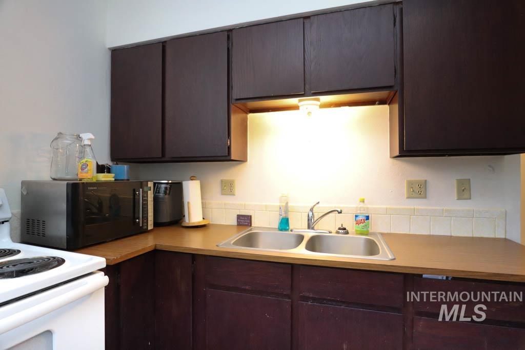 Kitchen with white range with electric cooktop, black microwave, dark brown cabinetry, and light countertops