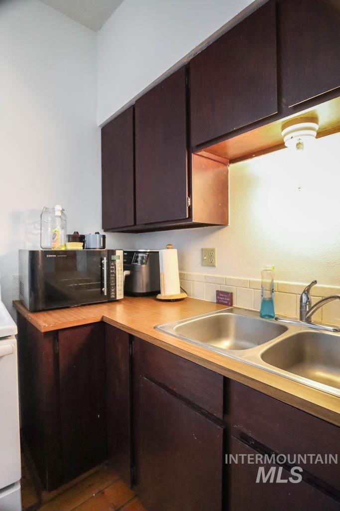 Kitchen with dark brown cabinetry, light countertops, black microwave, and white range oven
