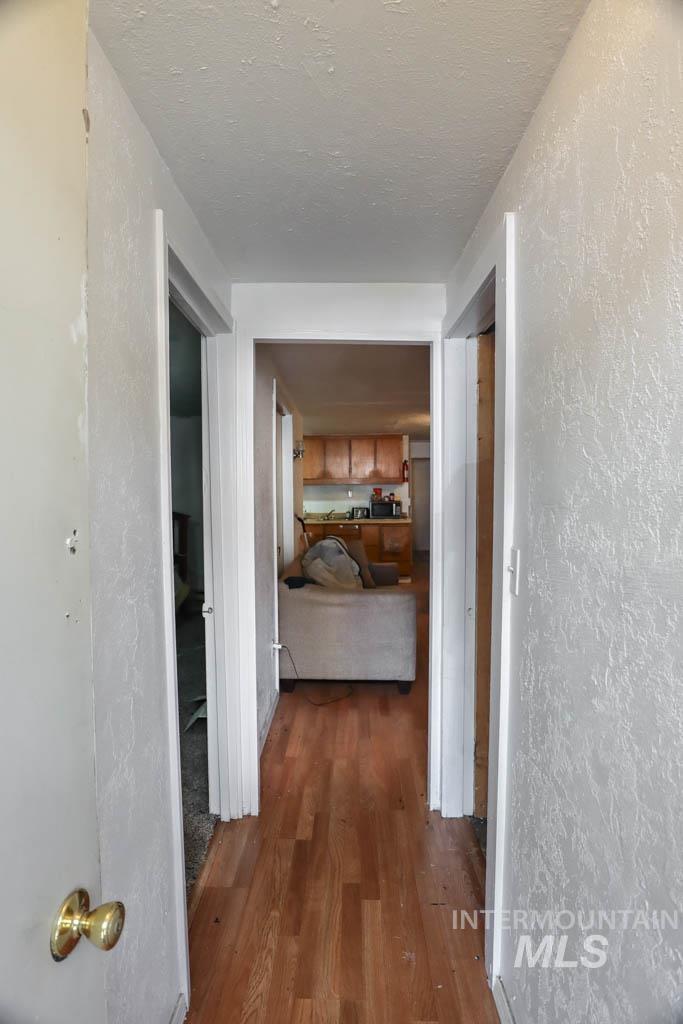 Corridor featuring a textured wall, dark wood finished floors, and a textured ceiling