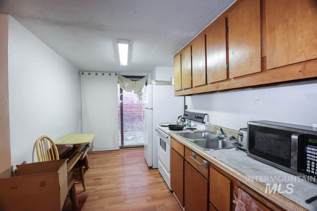 Kitchen featuring brown cabinets, light countertops, white range with electric stovetop, stainless steel microwave, and light wood finished floors