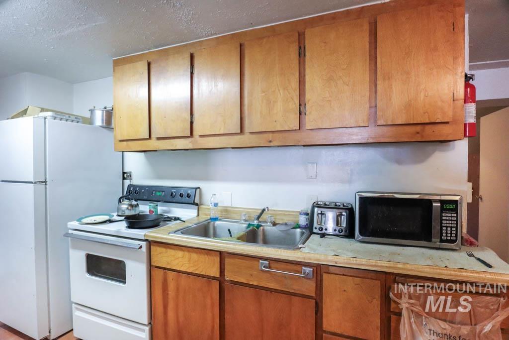 Kitchen featuring white appliances, light countertops, brown cabinetry, and a textured ceiling