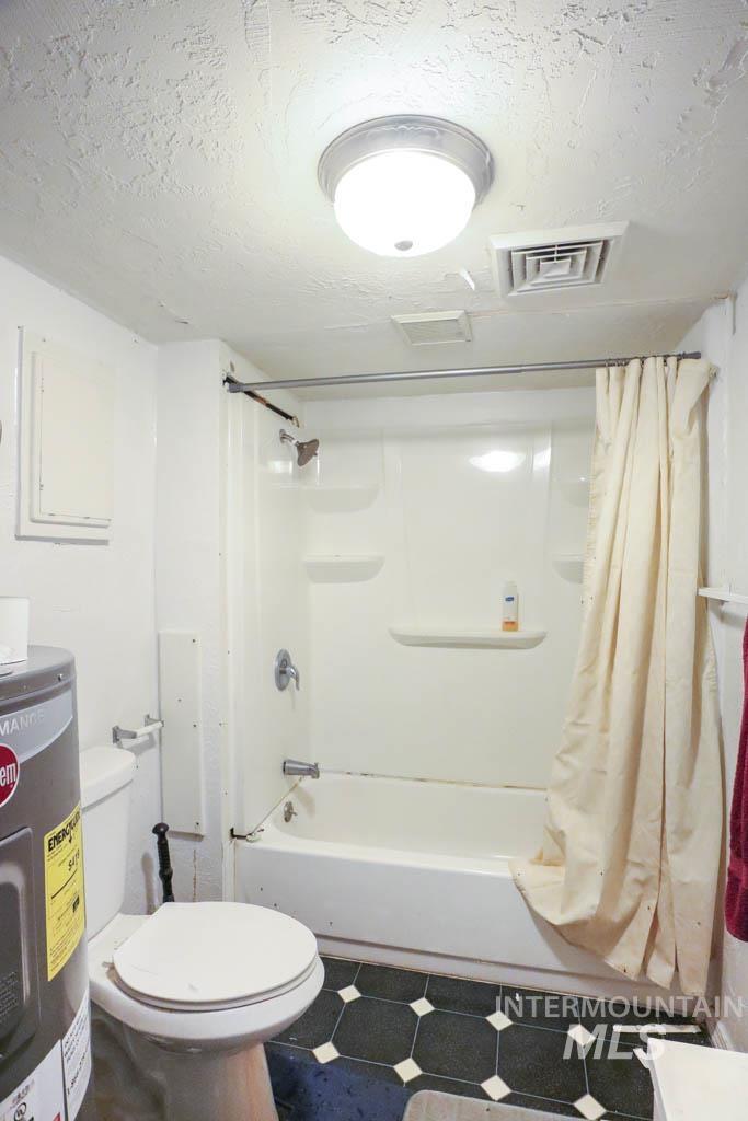 Full bath with shower / bath combination with curtain, a textured ceiling, water heater, and tile patterned floors