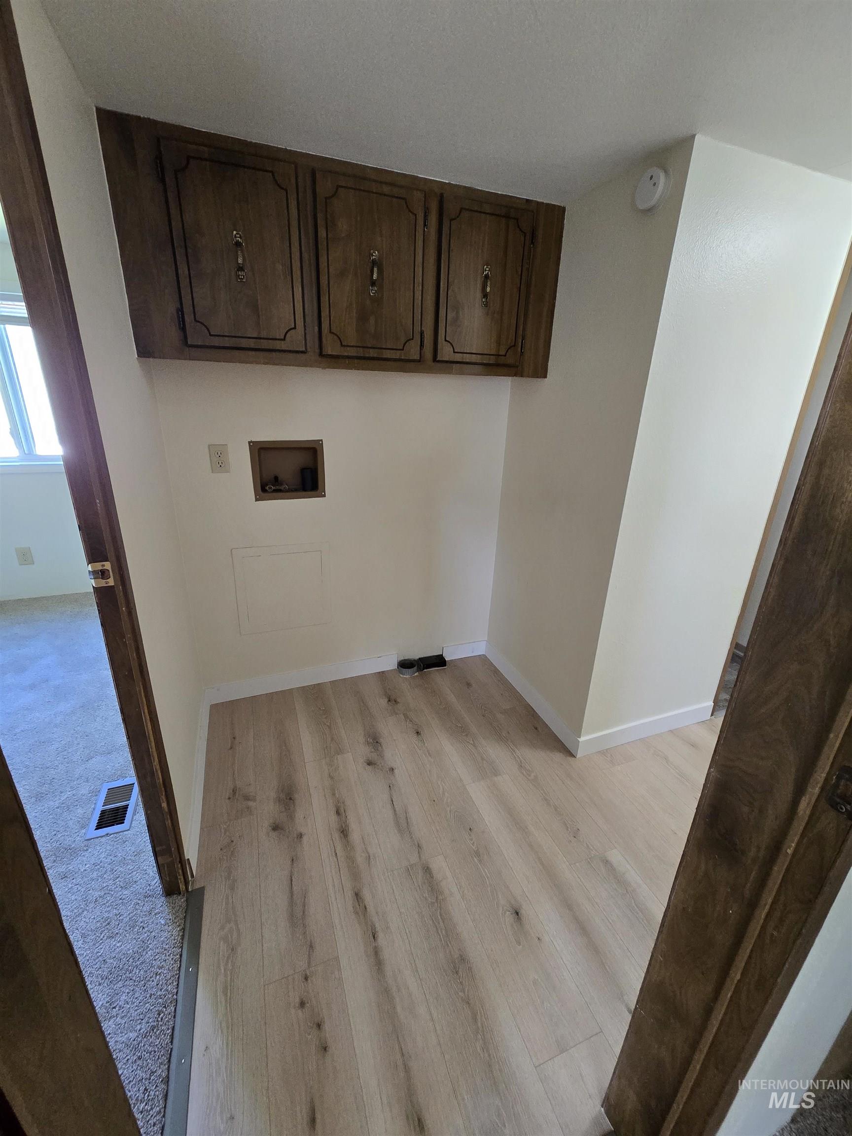 Laundry area with light wood-style floors, washer hookup, and cabinet space