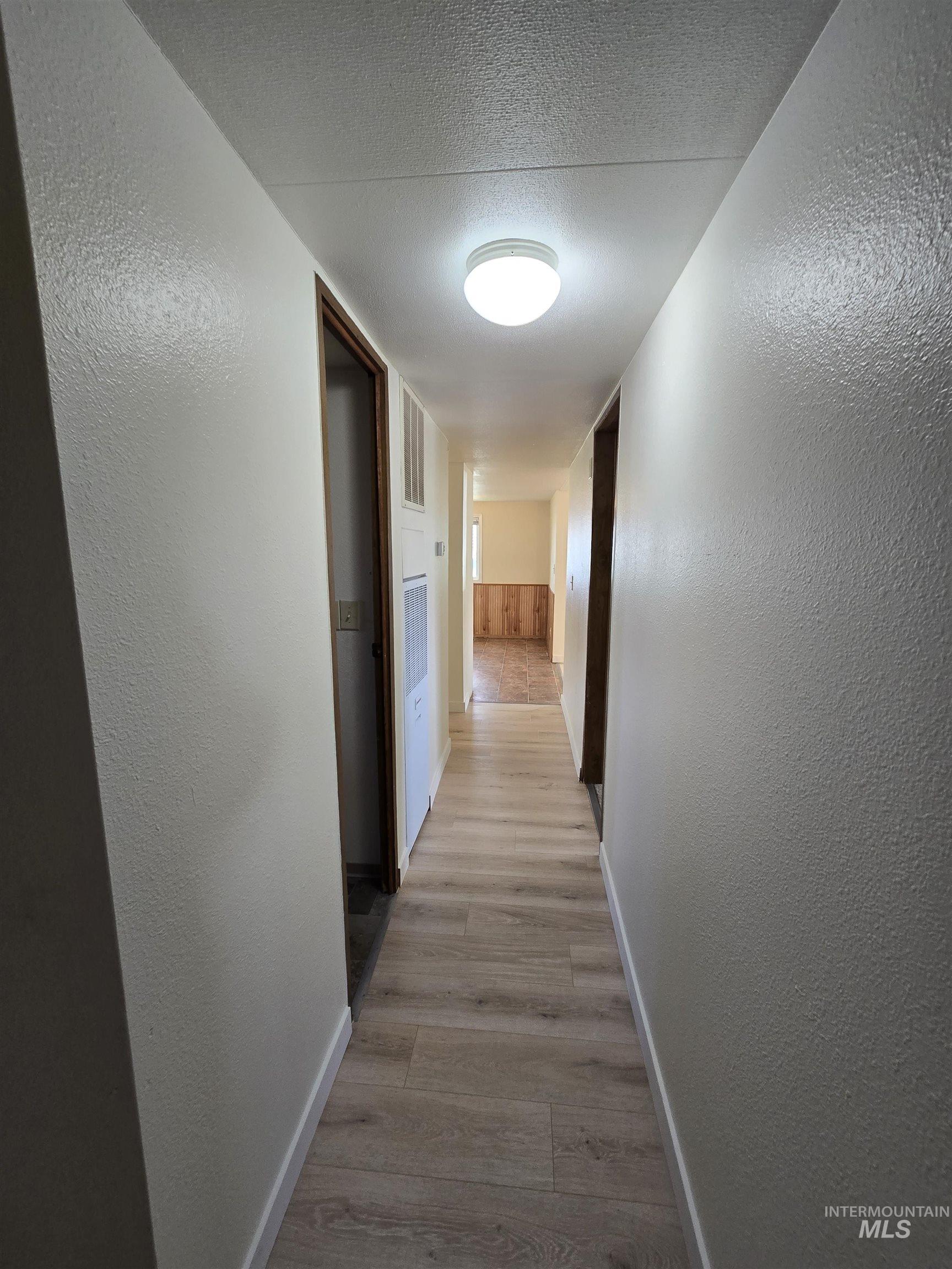 Hall featuring light wood-style floors, a textured wall, and a textured ceiling