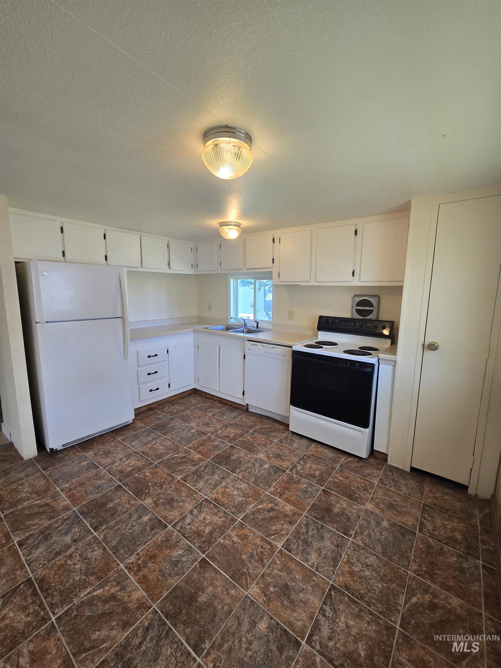 Kitchen with white appliances, light countertops, white cabinets, stone finish floors, and a textured ceiling