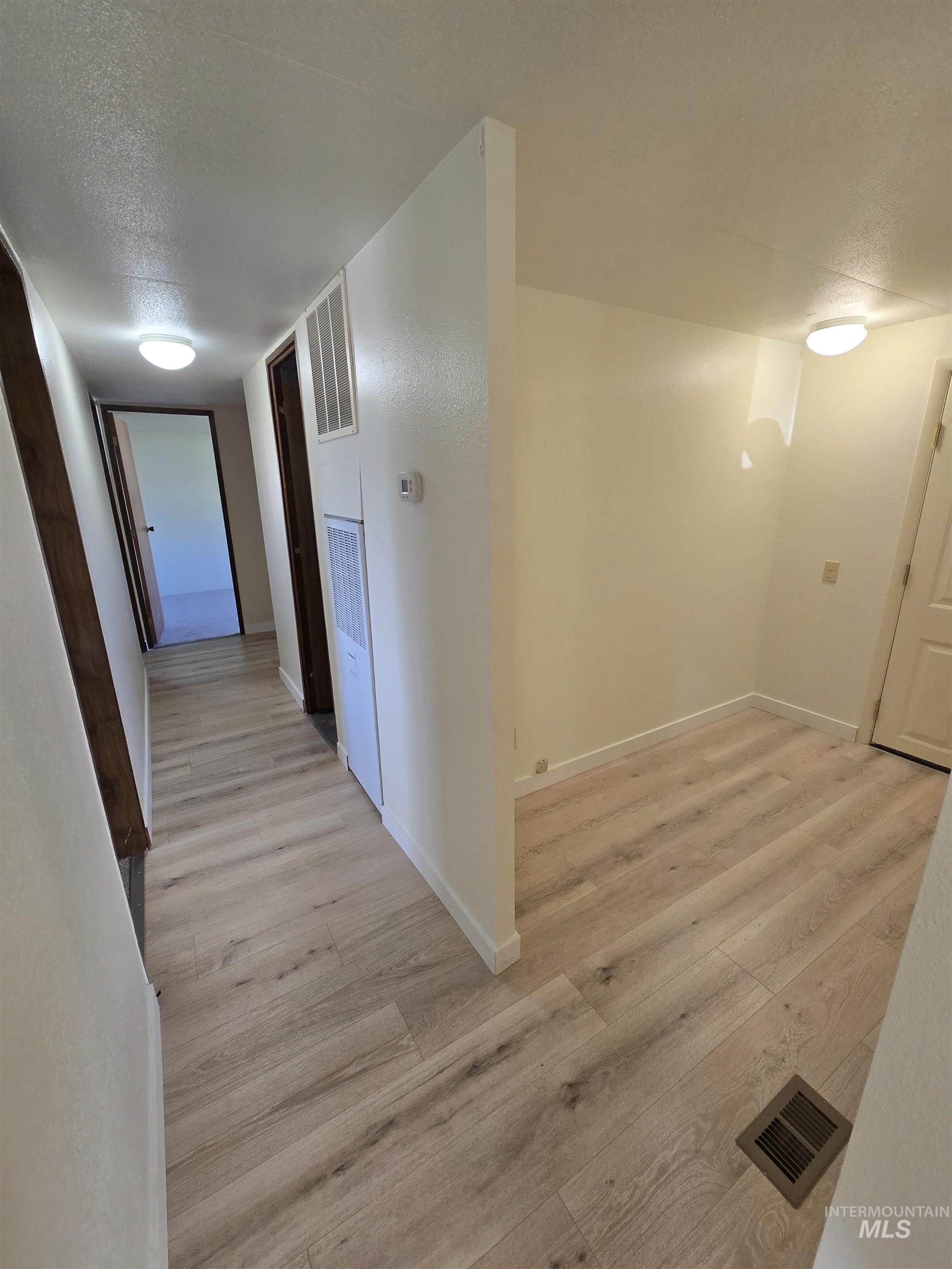 Corridor featuring a textured ceiling, light wood finished floors, and a heating unit