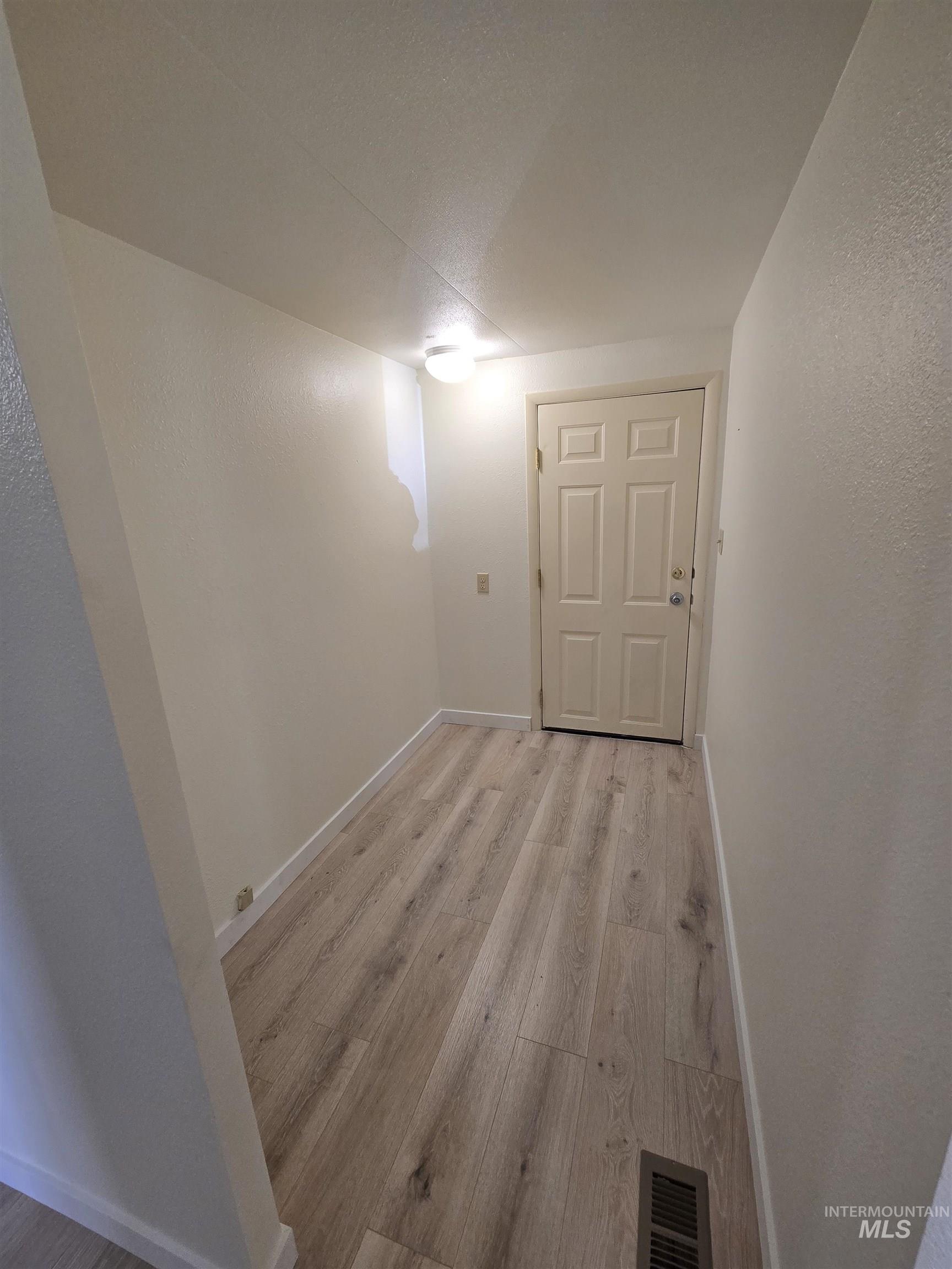 Finished below grade area with light wood-type flooring and a textured wall