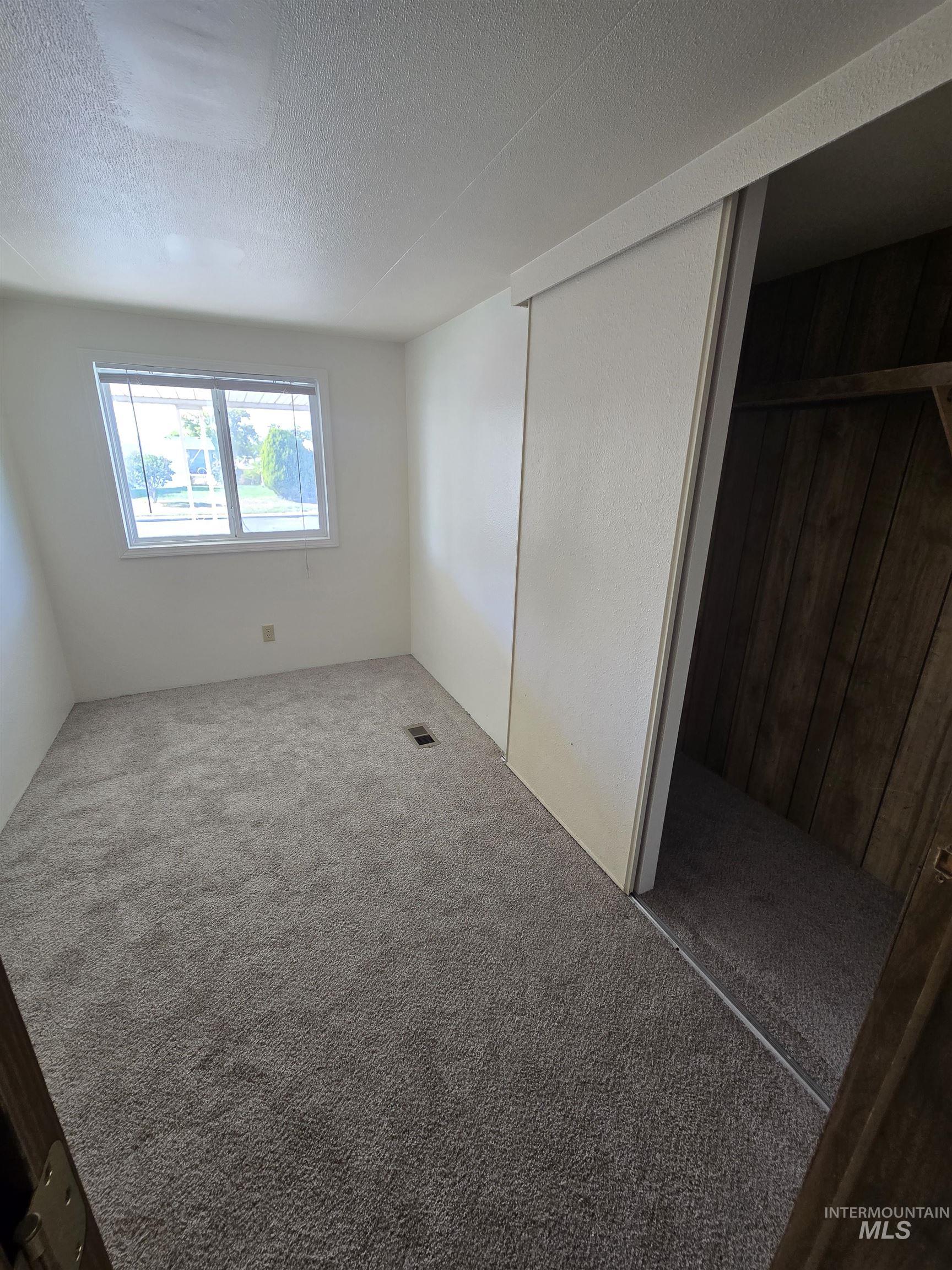 Unfurnished bedroom with a textured ceiling, carpet floors, a closet, and wood walls