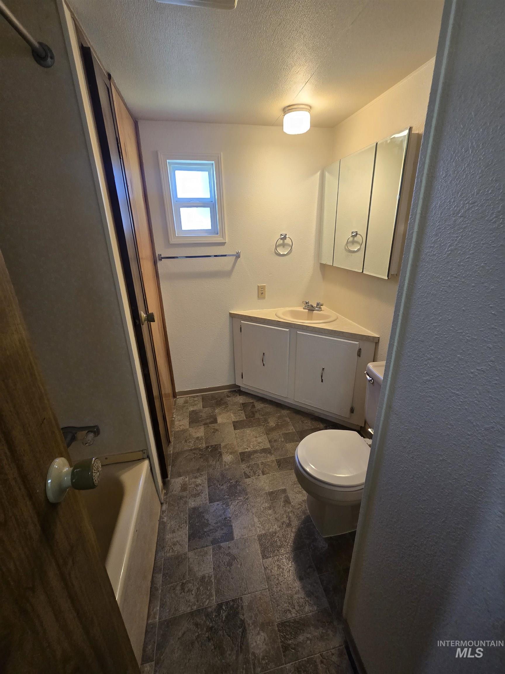 Bathroom featuring stone finish flooring, vanity, a textured ceiling, and  shower combination
