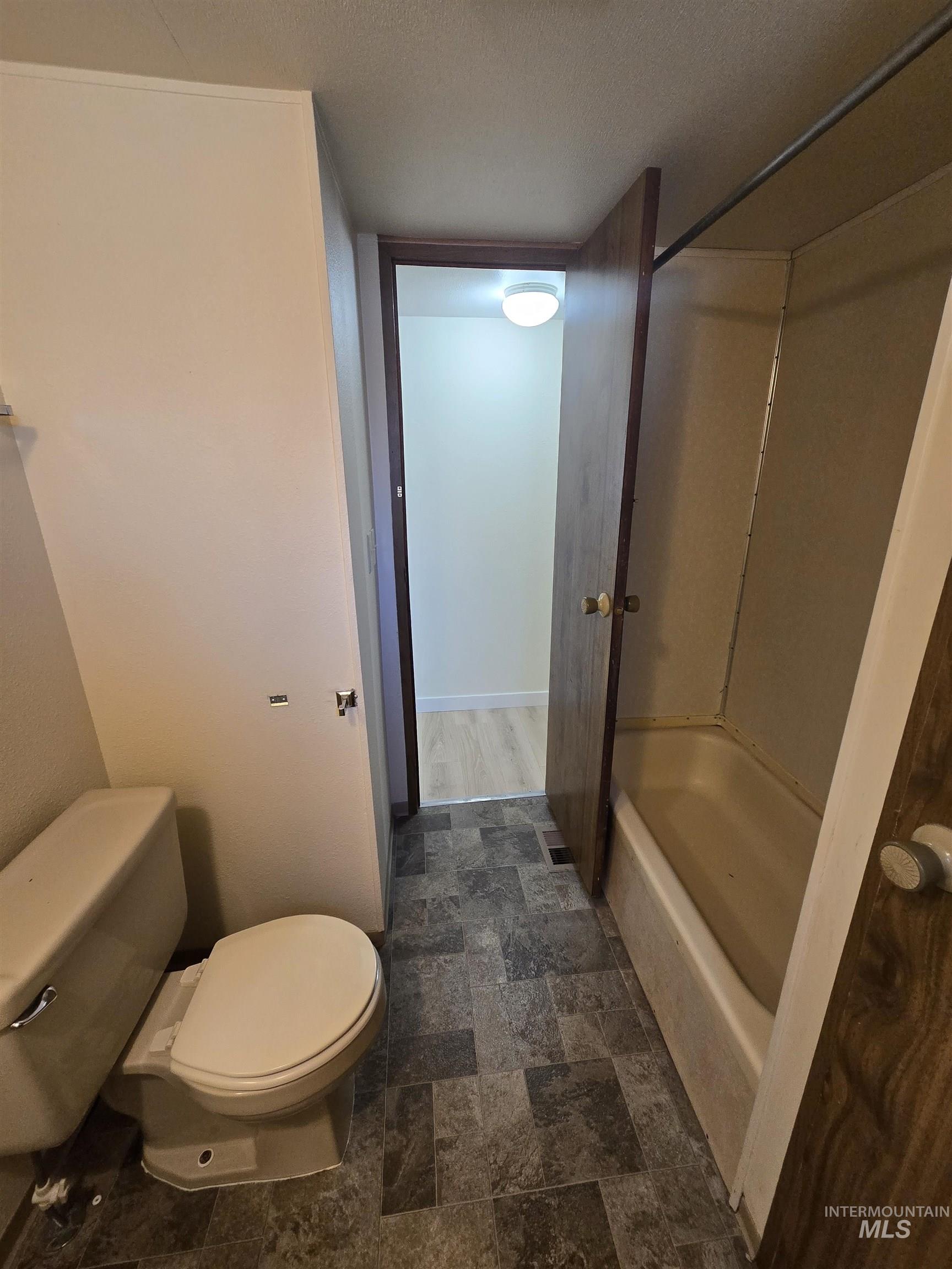 Bathroom with stone finish floors, tub / shower combination, and a textured ceiling