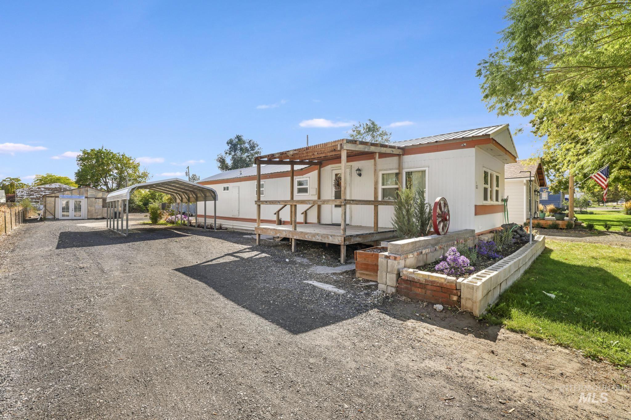 View of front facade featuring a detached carport, dirt driveway, a wooden deck, a metal roof, and an outdoor structure
