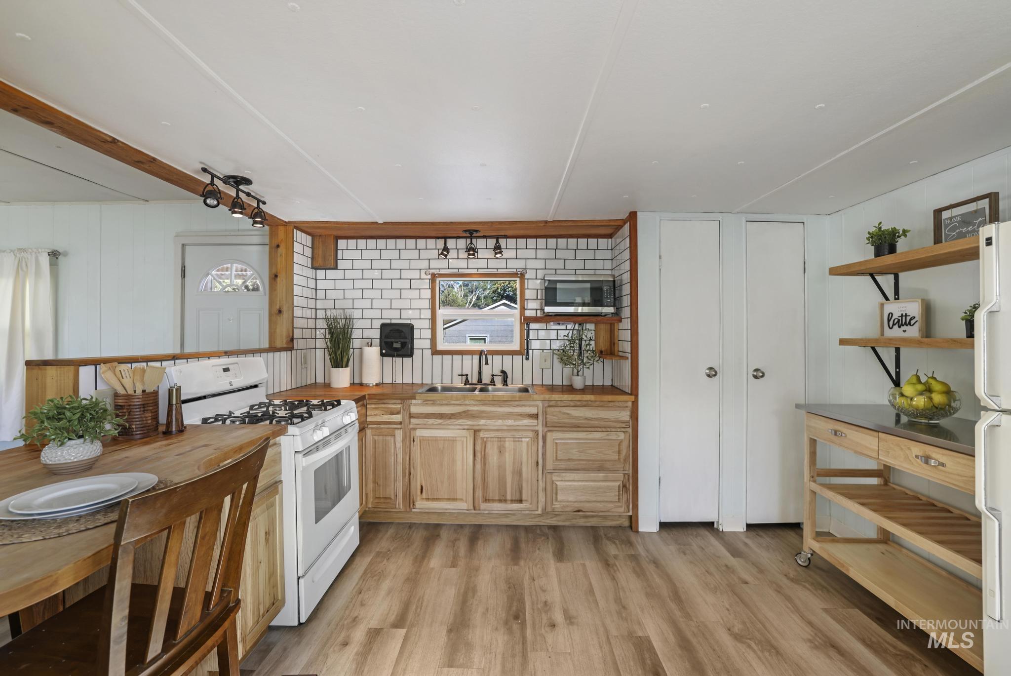 Kitchen with white appliances, light brown cabinetry, light wood-style flooring, wooden counters, and backsplash