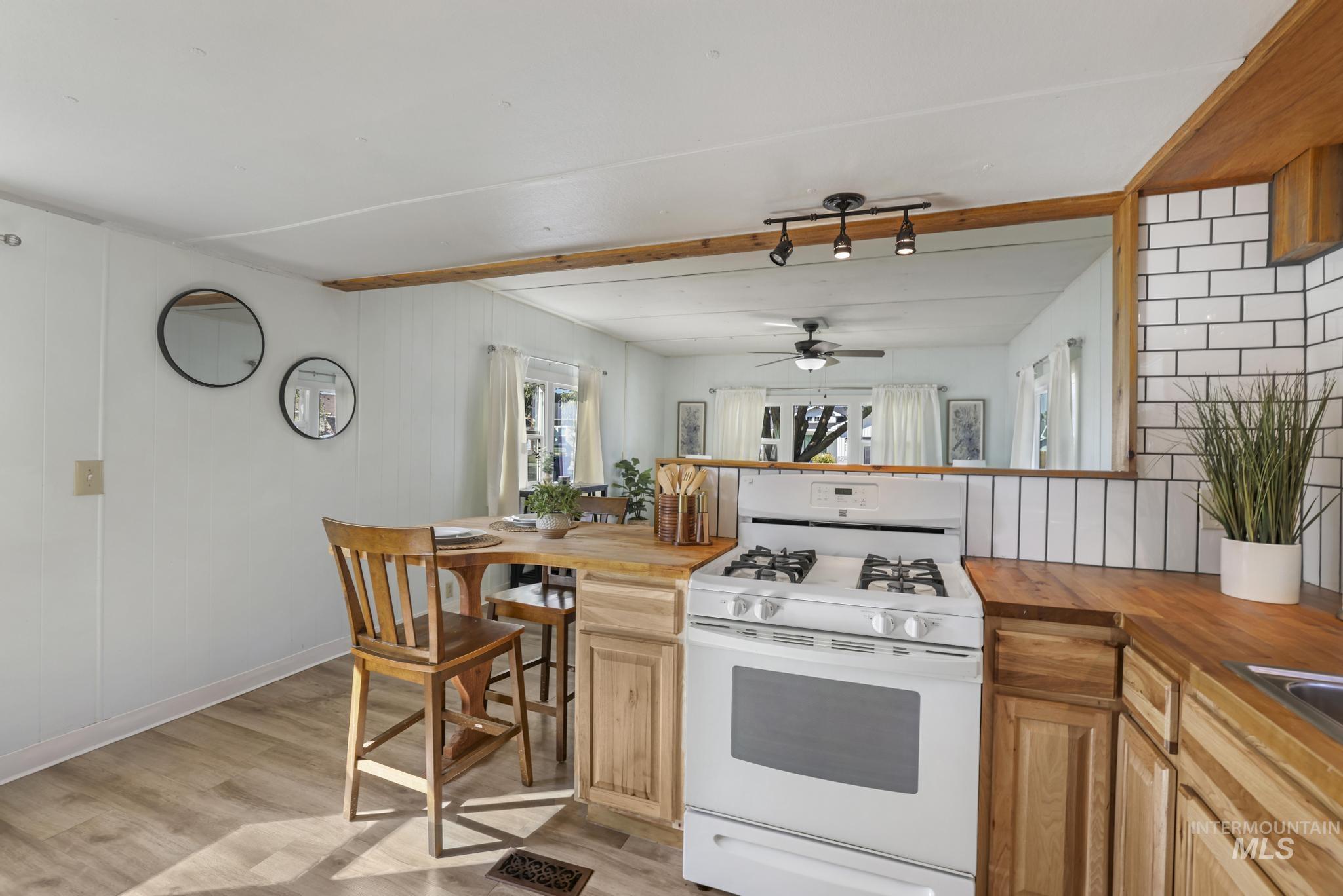 Kitchen with white gas range oven, light wood-style floors, butcher block countertops, a ceiling fan, and a peninsula