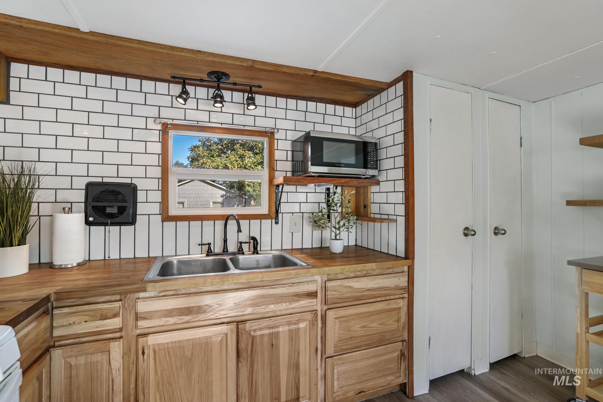 Kitchen with dark wood-style floors, tasteful backsplash, stainless steel microwave, light brown cabinets, and wood counters