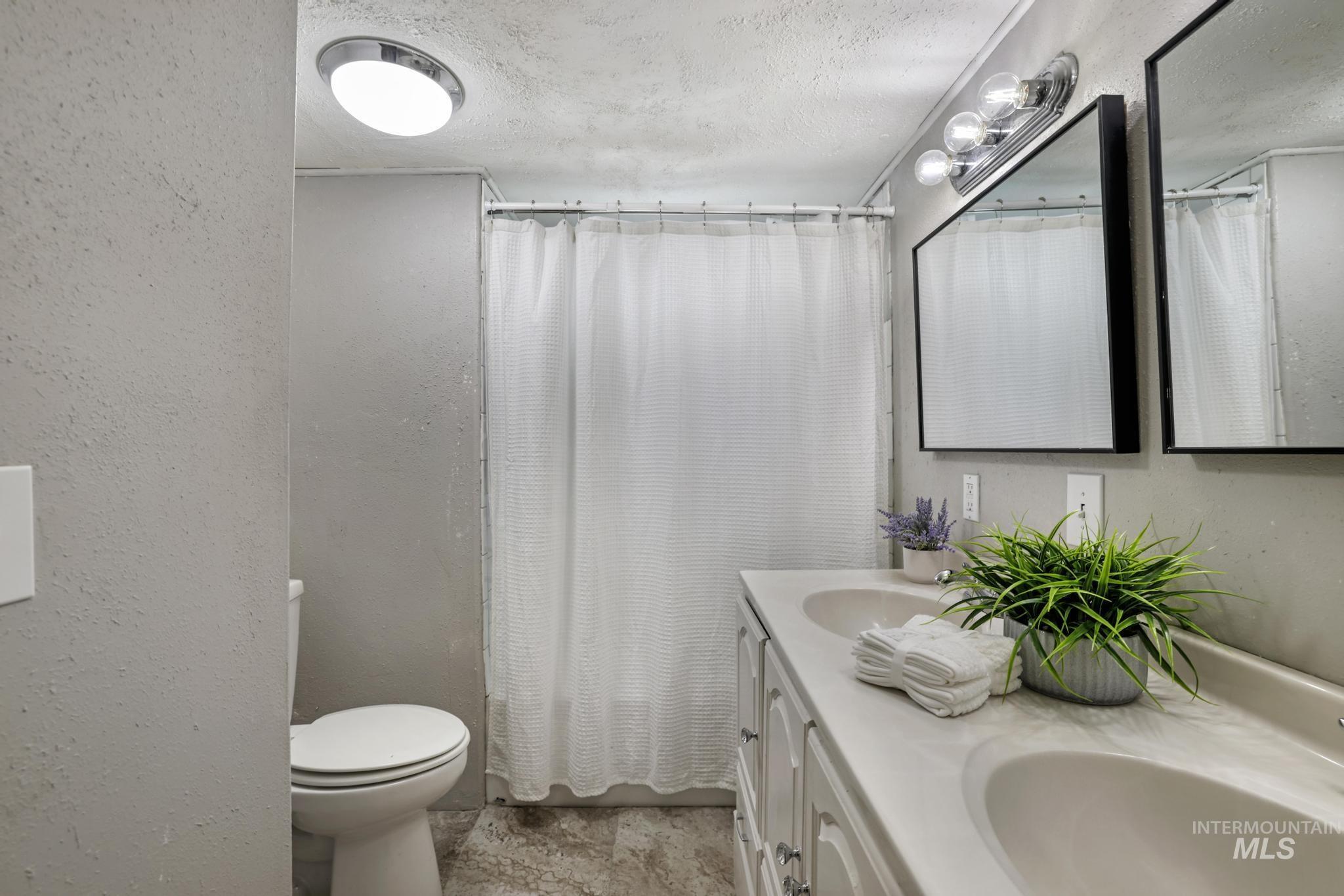 Bathroom featuring double vanity, a textured wall, a textured ceiling, and a shower with curtain