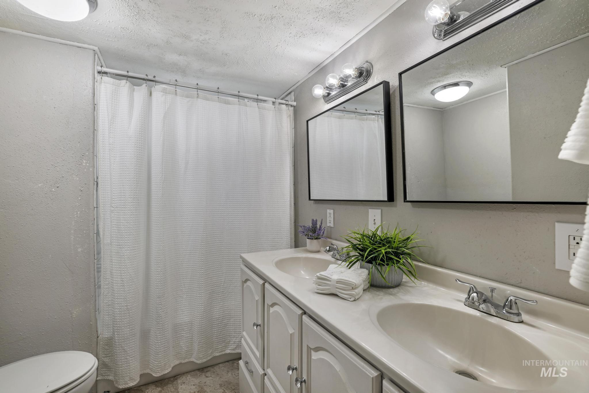 Full bathroom featuring a textured ceiling, double vanity, a textured wall, and shower / bath combination with curtain