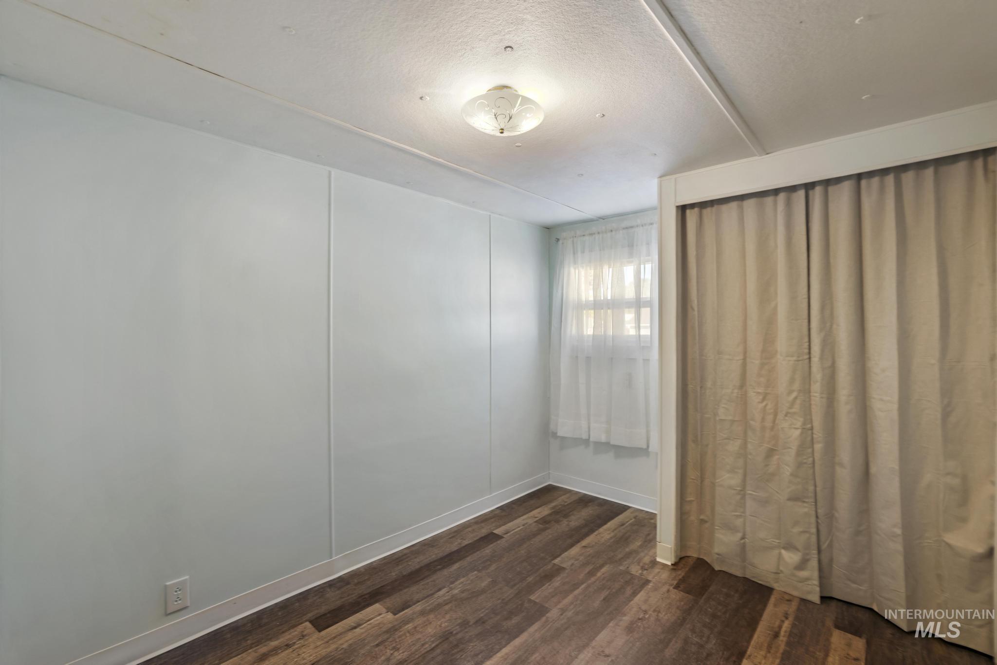 Unfurnished bedroom with dark wood-style floors, a textured ceiling, and a decorative wall