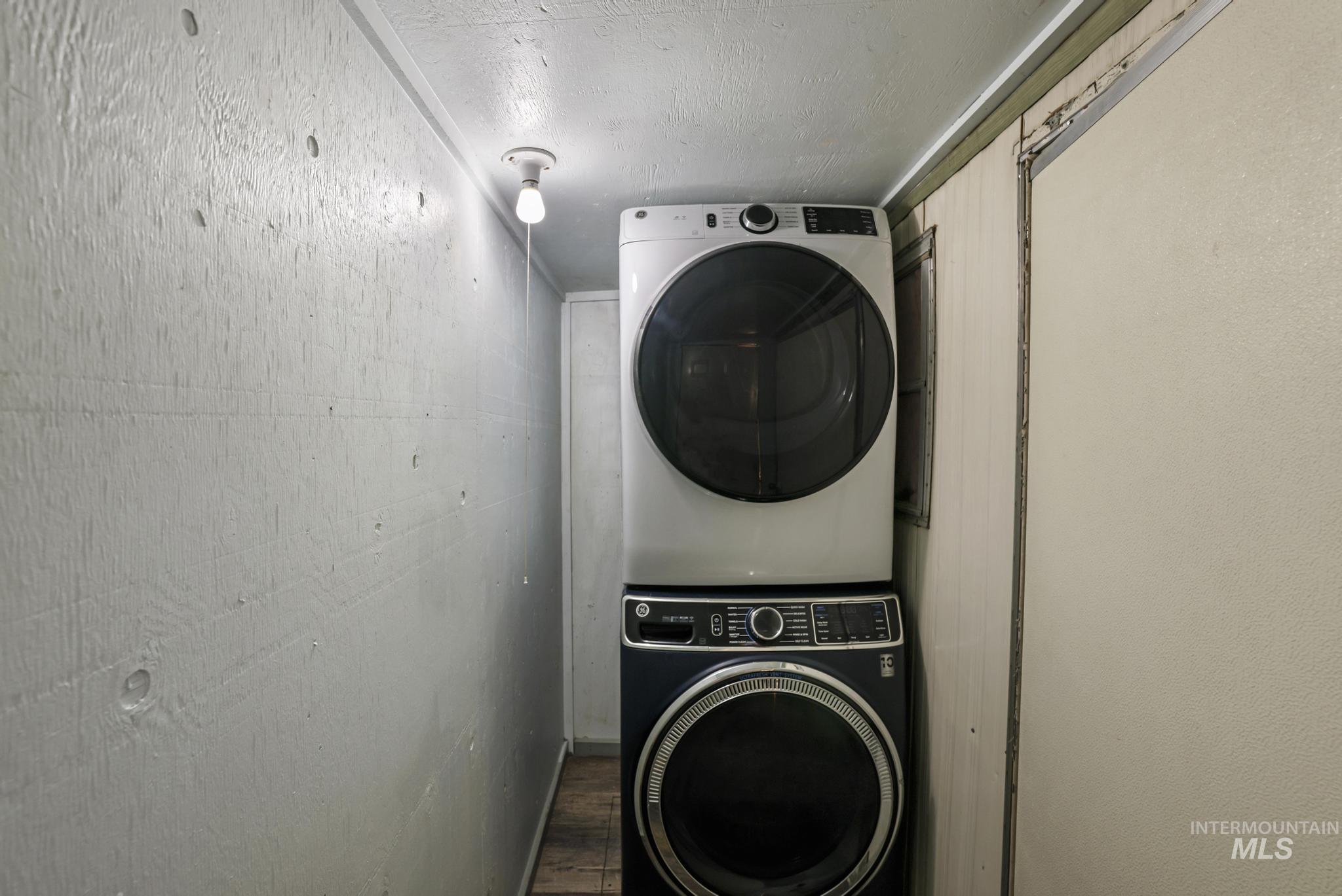 Washroom with estacked washer and dryer, a textured ceiling, and wood finished floors