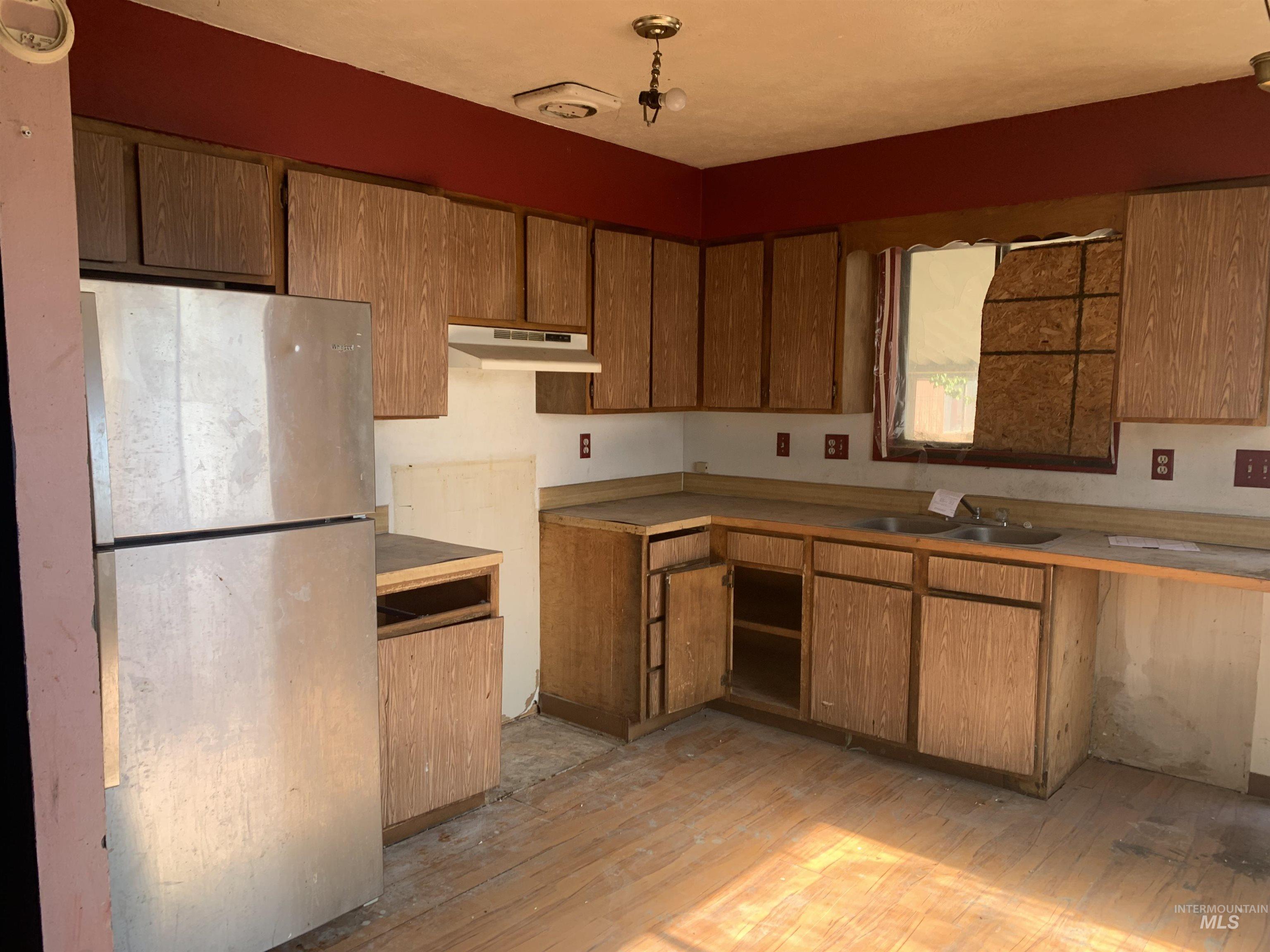 Kitchen with freestanding refrigerator, light wood-type flooring, brown cabinetry, under cabinet range hood, and light countertops