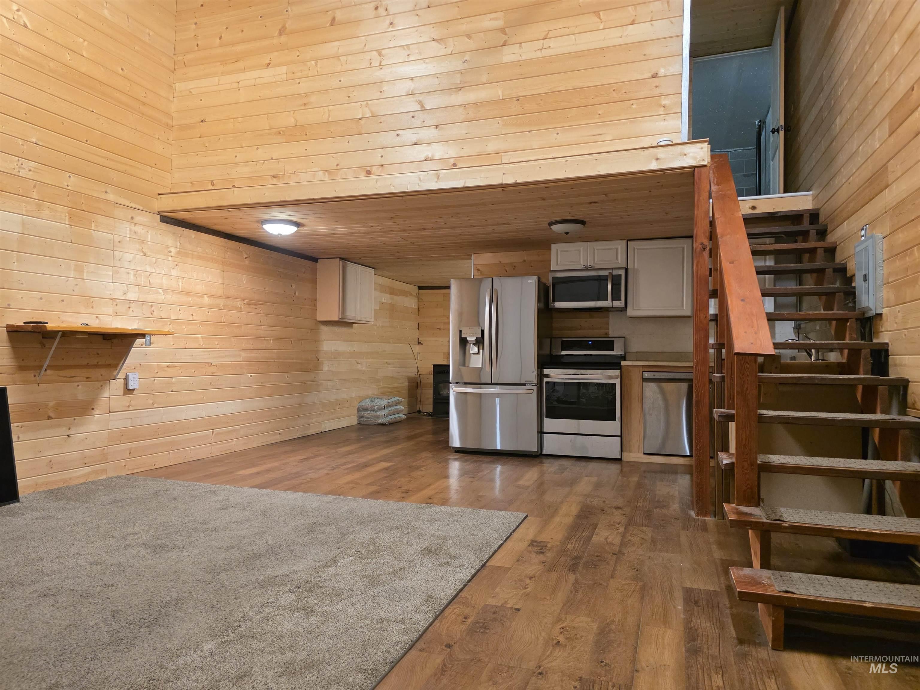 Kitchen with wooden walls, appliances with stainless steel finishes, wood finished floors, a towering ceiling, and light countertops