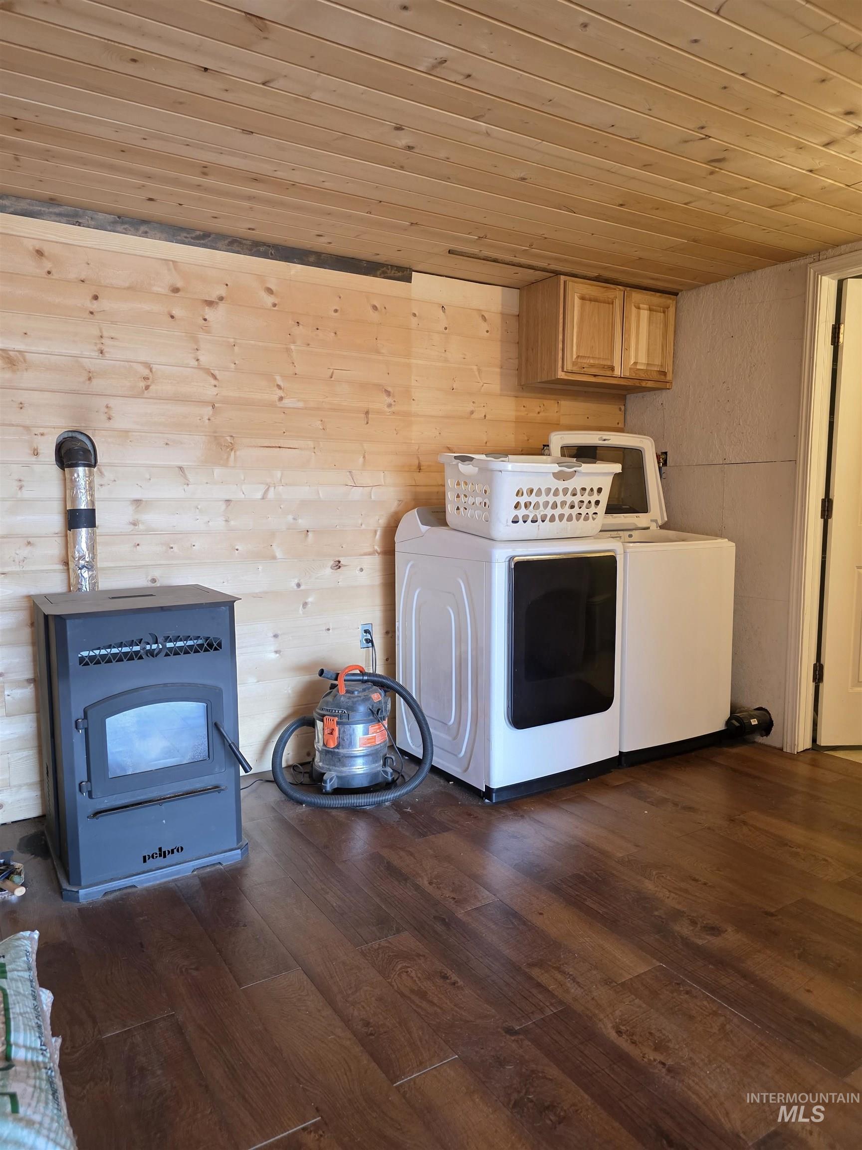 Washroom with wooden ceiling, dark wood-type flooring, cabinet space, washing machine and clothes dryer, and a wood stove