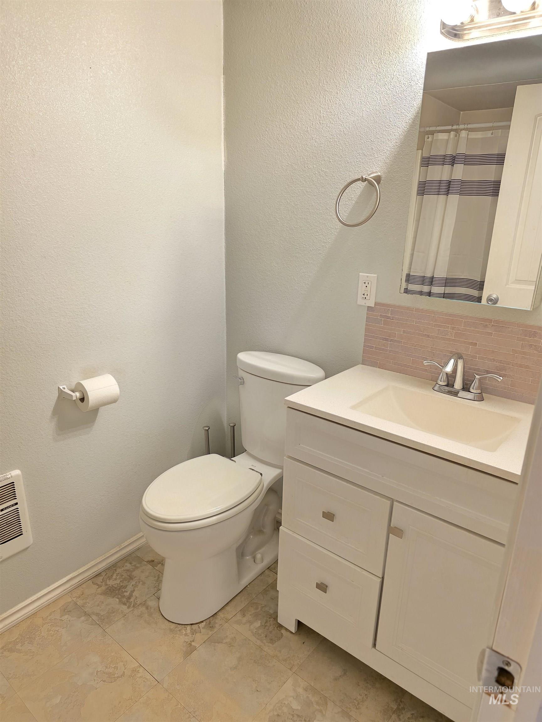 Bathroom featuring a textured wall, vanity, decorative backsplash, and a shower with shower curtain