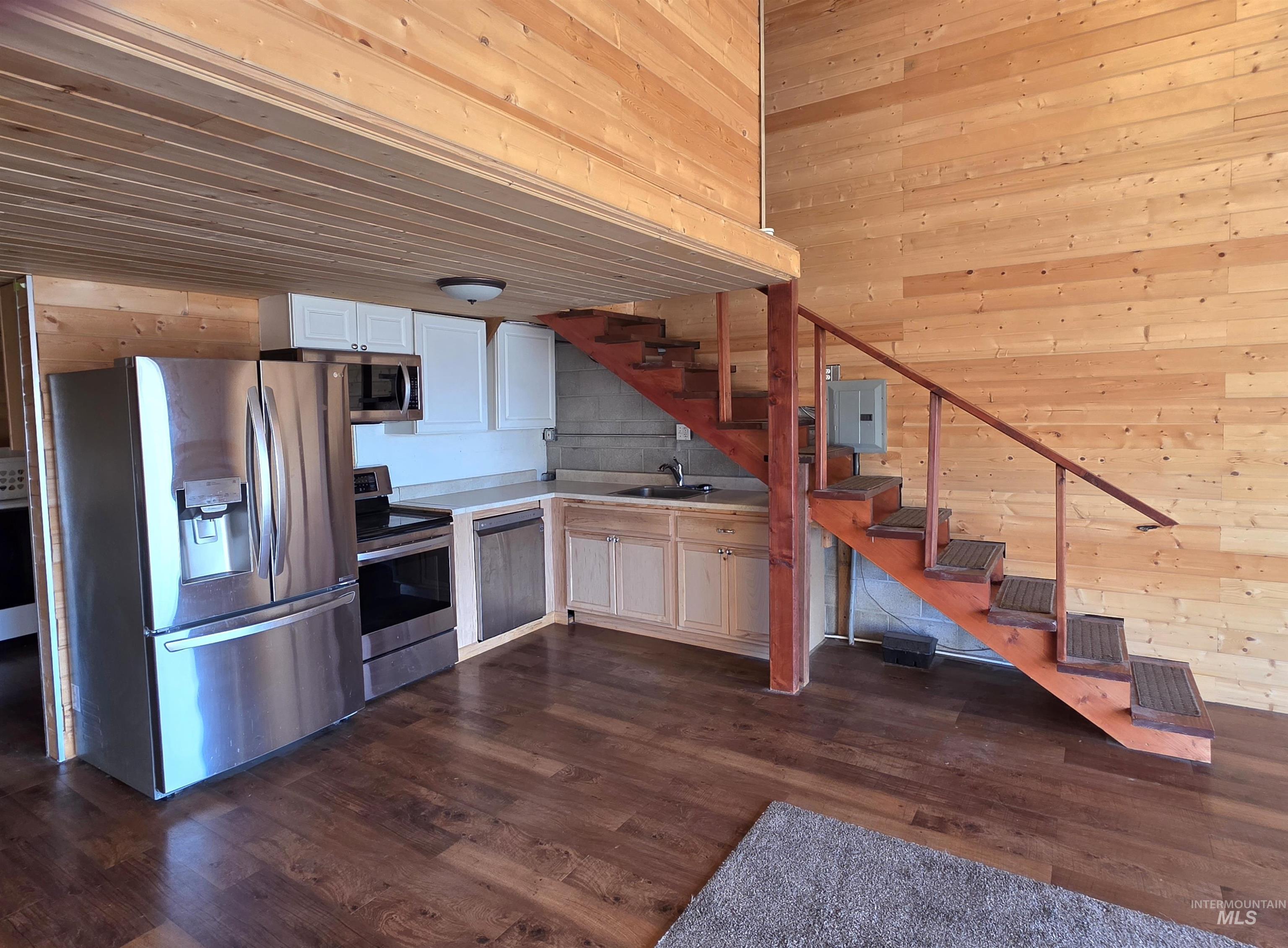 Kitchen with wood walls, stainless steel appliances, light countertops, dark wood-type flooring, and electric panel