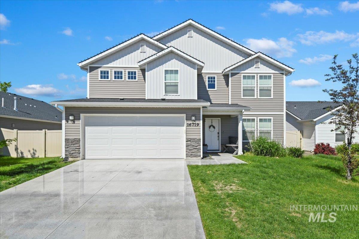 View of front facade featuring board and batten siding, a garage, driveway, and stone siding