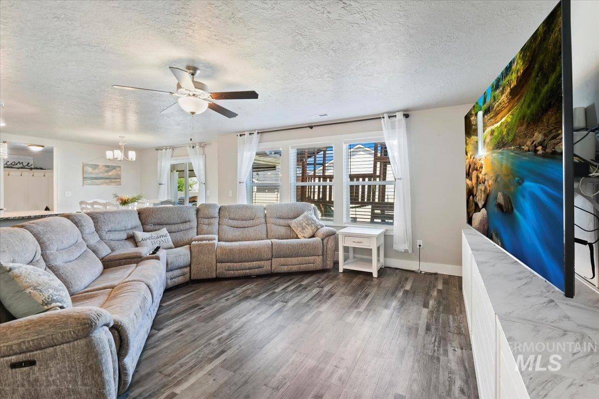Living room with a textured ceiling, a ceiling fan, dark wood-style flooring, and a chandelier