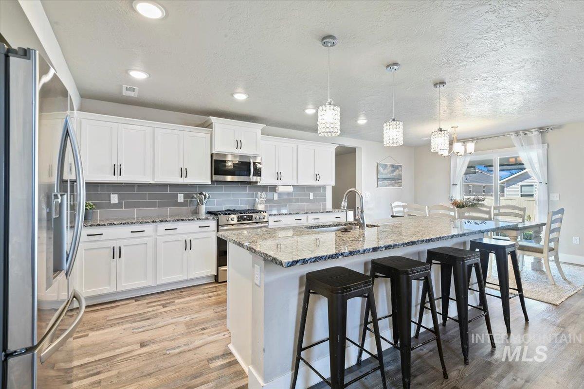 Kitchen with backsplash, appliances with stainless steel finishes, decorative light fixtures, light stone countertops, and a breakfast bar area