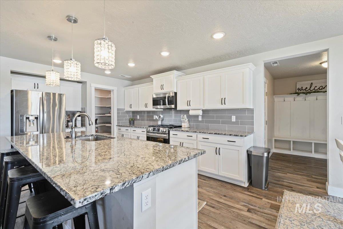 Kitchen featuring decorative backsplash, appliances with stainless steel finishes, light stone counters, white cabinets, and pendant lighting