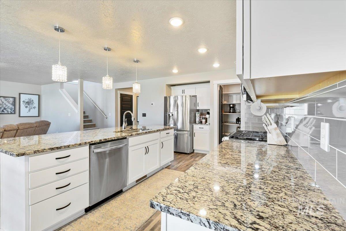 Kitchen featuring appliances with stainless steel finishes, white cabinets, a textured ceiling, hanging light fixtures, and light stone counters