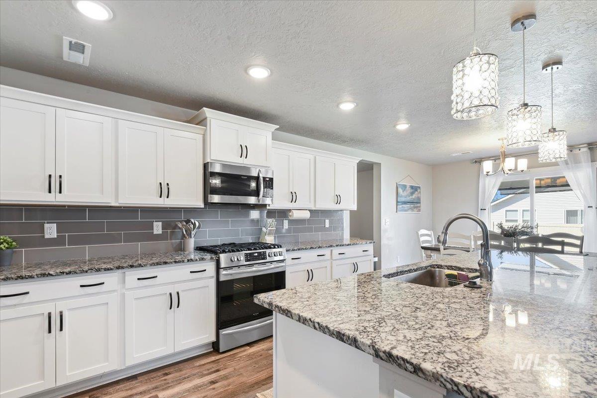 Kitchen featuring stainless steel appliances, white cabinets, hanging light fixtures, backsplash, and light stone counters