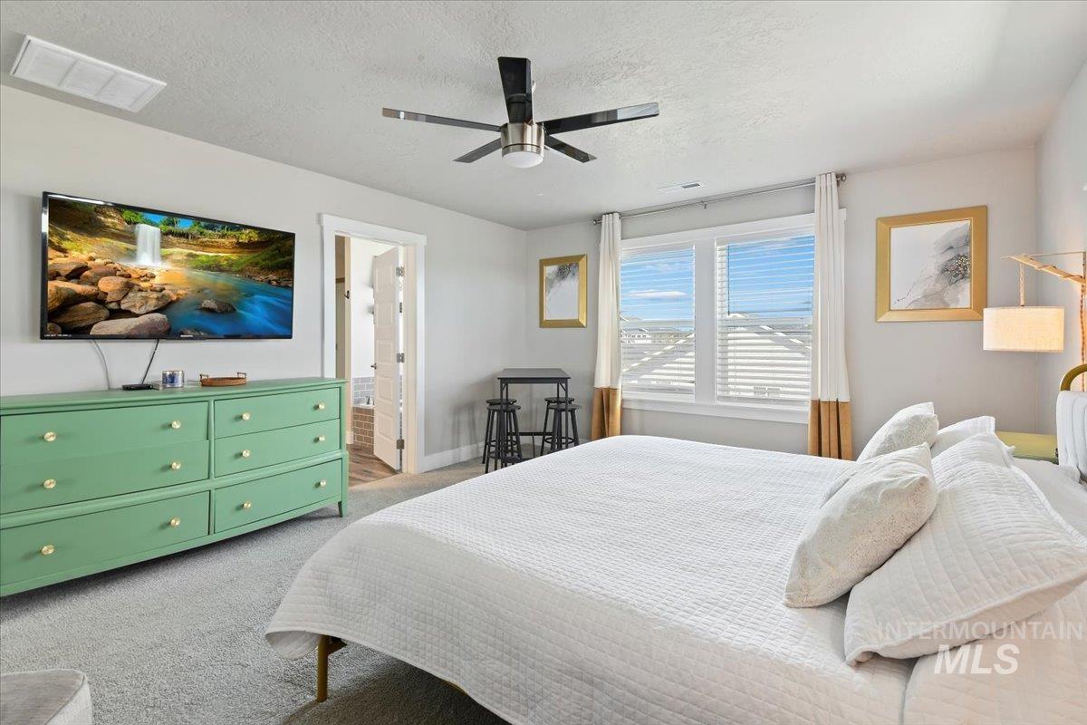 Bedroom with a textured ceiling, carpet floors, a ceiling fan, and ensuite bath