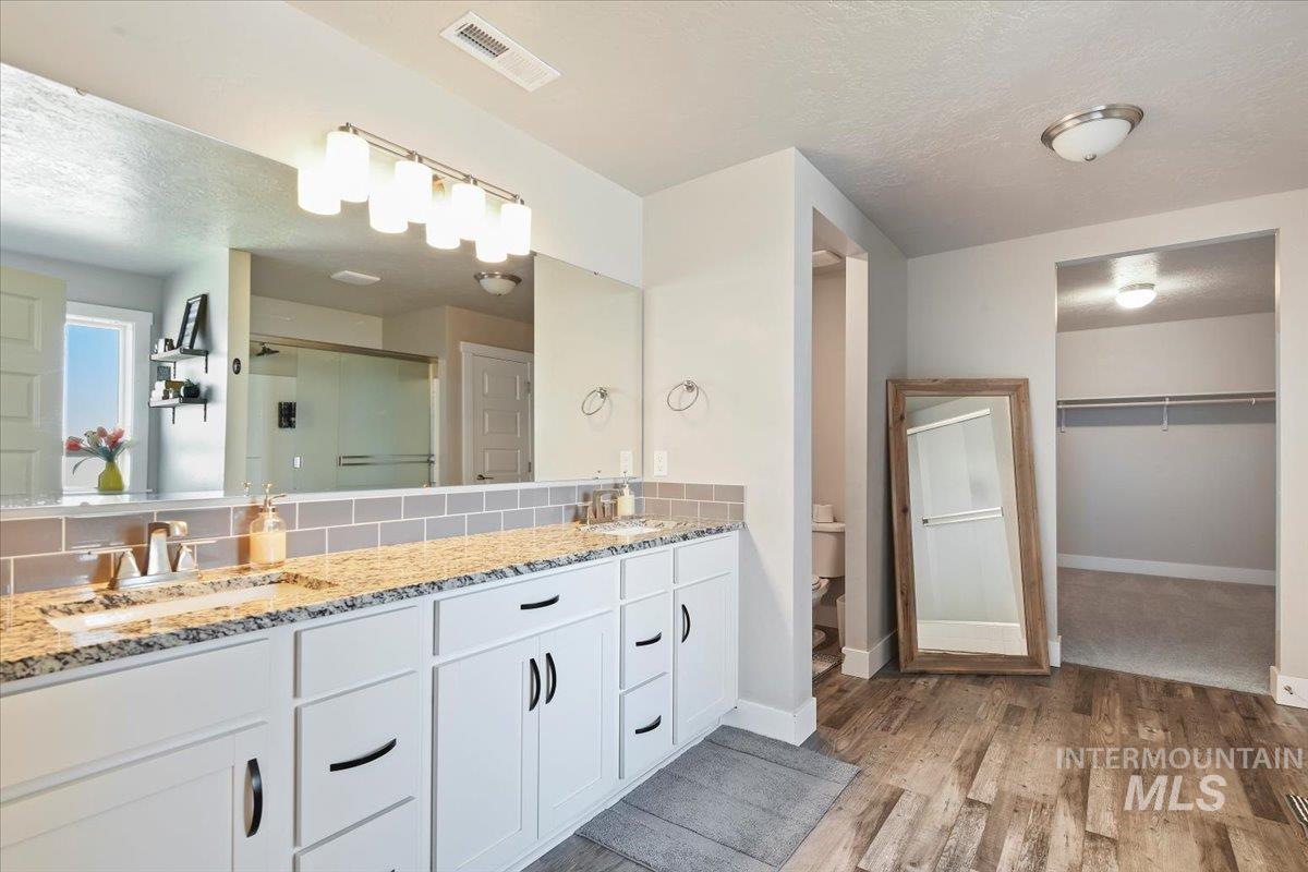 Bathroom with a textured ceiling, light wood-style flooring, double vanity, a stall shower, and a spacious closet