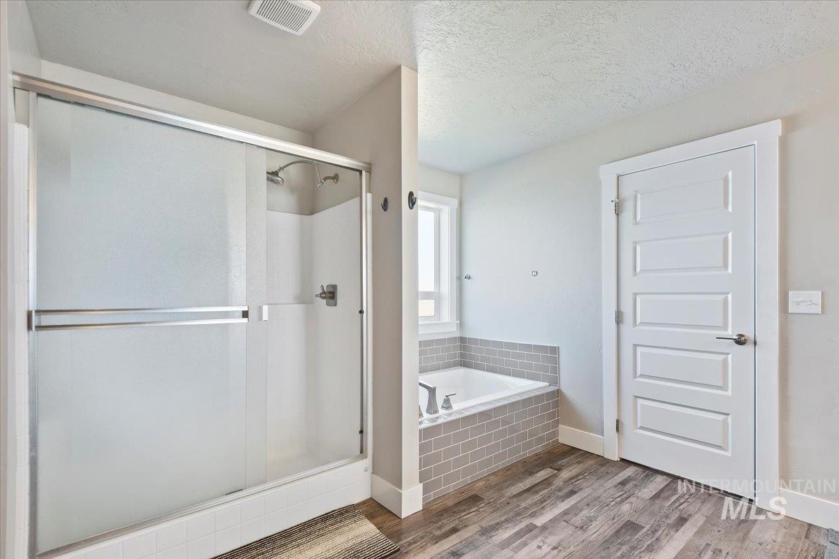 Full bathroom featuring a textured ceiling, a shower stall, light wood-style flooring, and a garden tub
