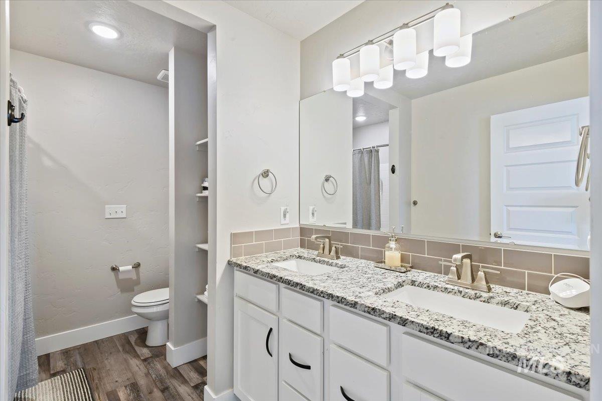 Full bath with dark wood-style flooring, backsplash, double vanity, and a shower with curtain