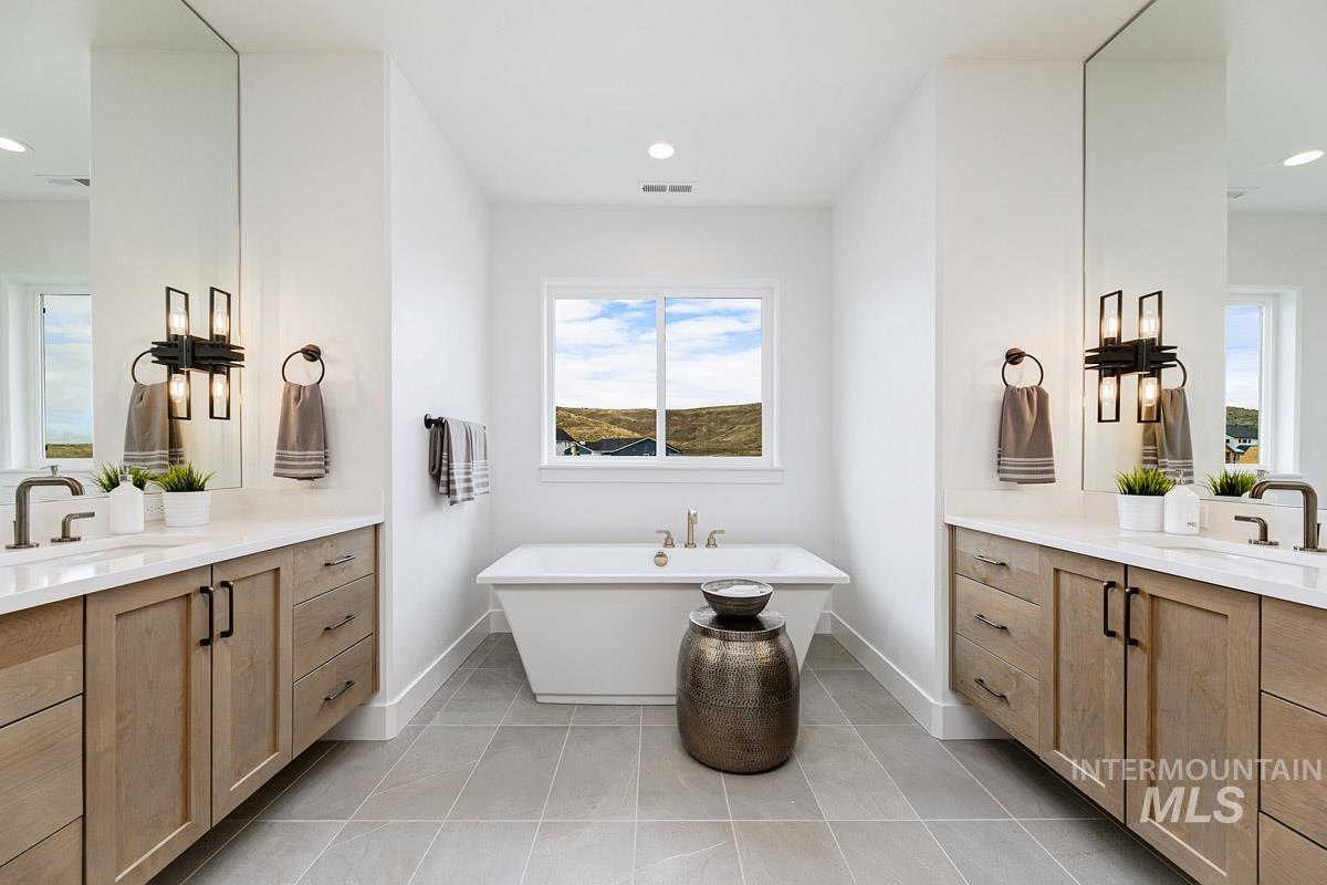 Full bathroom with a freestanding tub, two vanities, light tile patterned floors, and recessed lighting