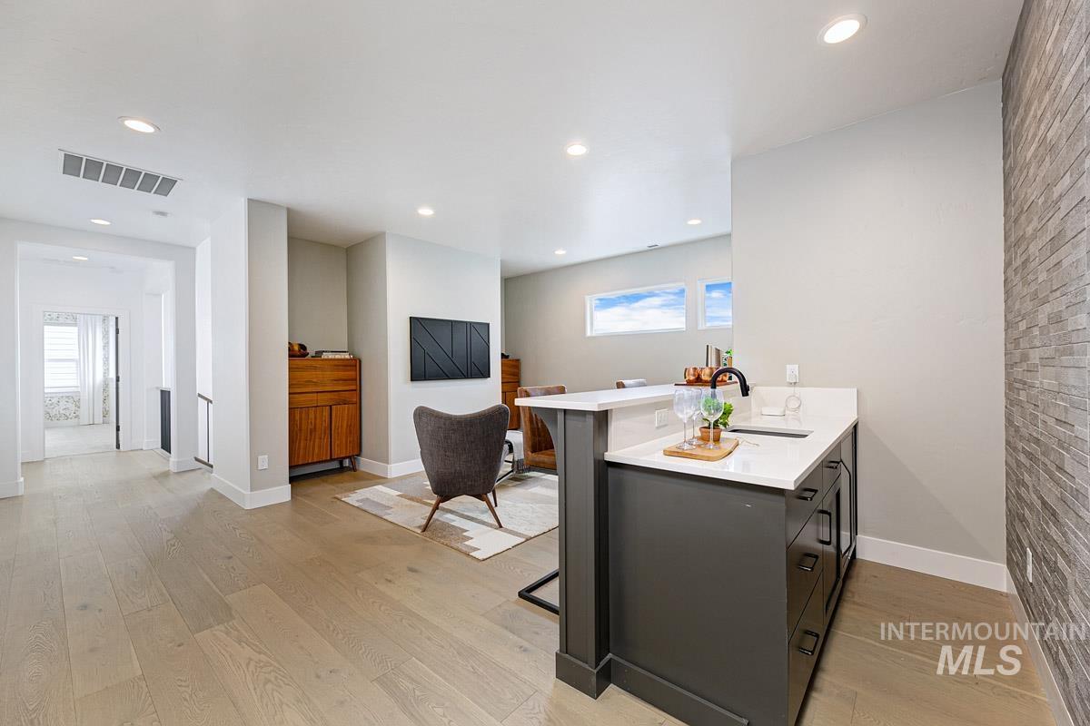 Kitchen featuring a peninsula, light wood-type flooring, a kitchen breakfast bar, light stone counters, and recessed lighting