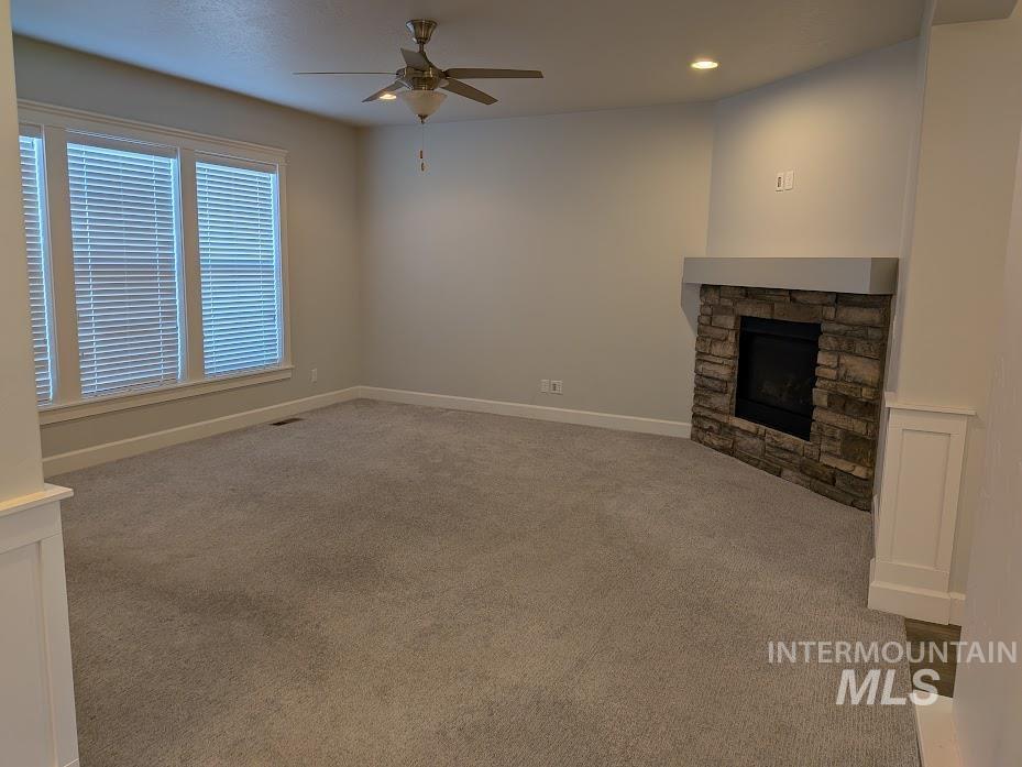 Unfurnished living room with a stone fireplace, carpet flooring, ceiling fan, and recessed lighting