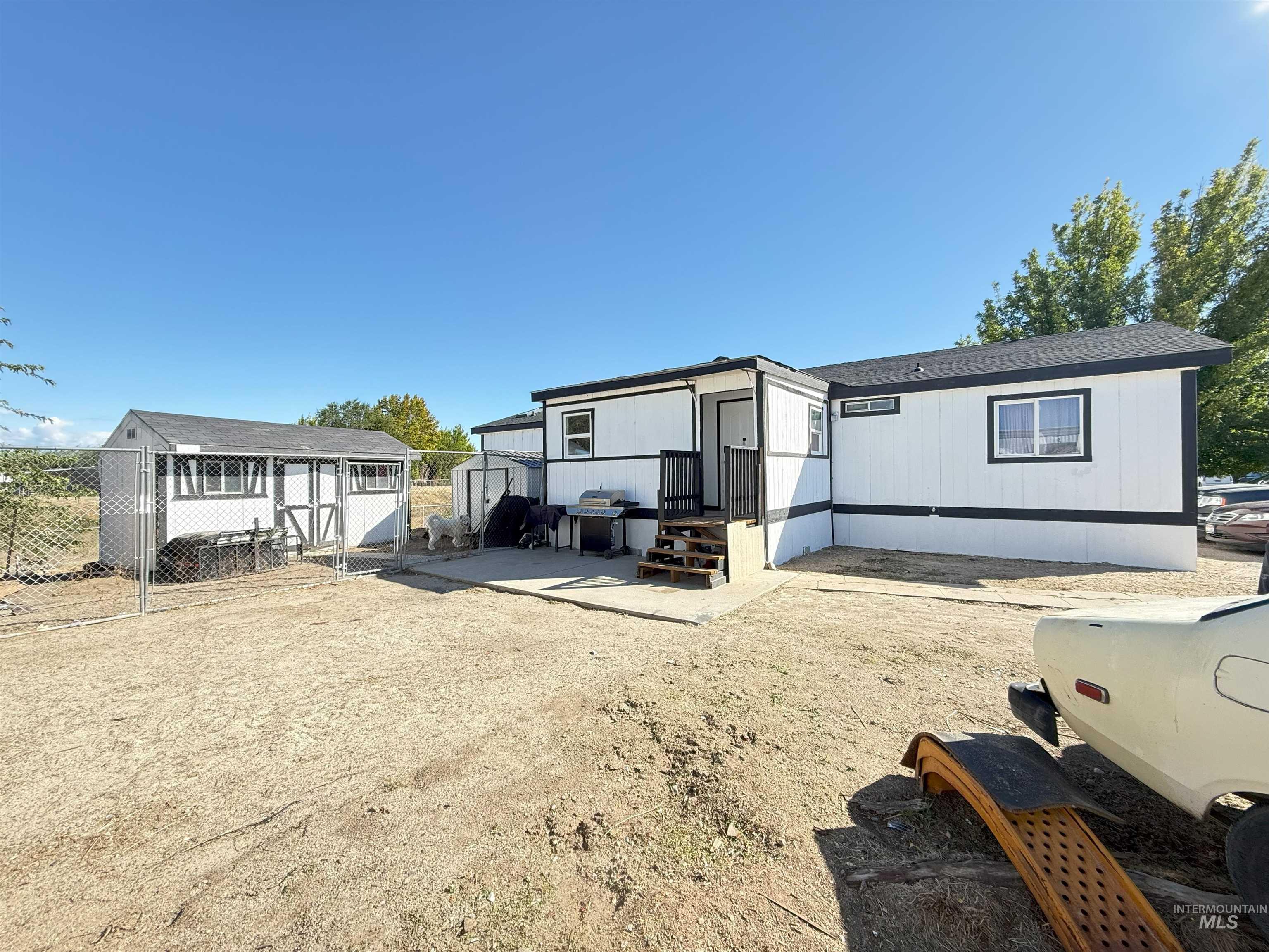 View of front of home with a patio area, a shingled roof, and a storage unit