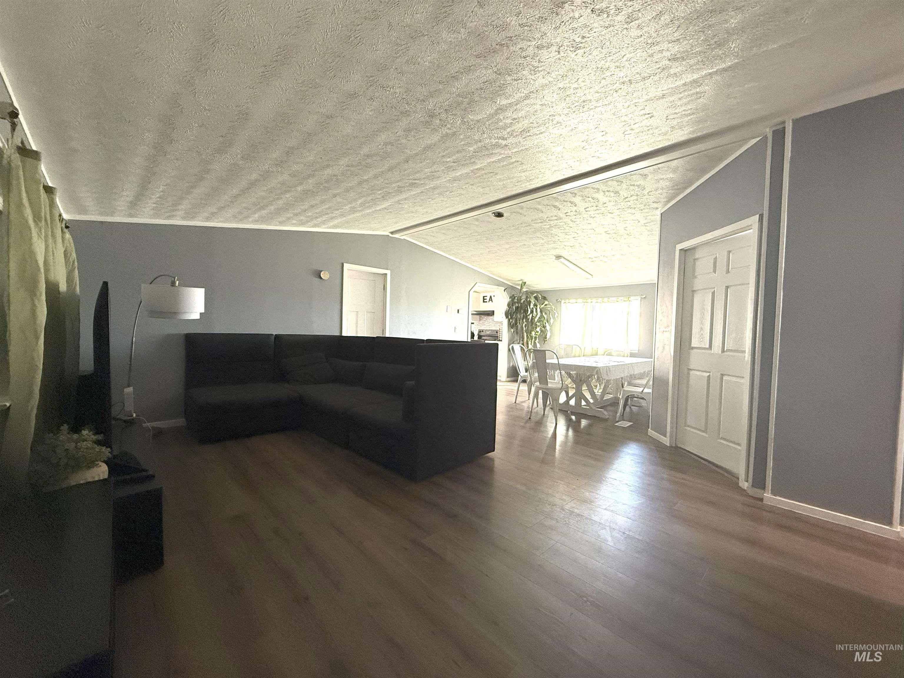 Living room featuring a textured ceiling, dark wood-type flooring, and vaulted ceiling