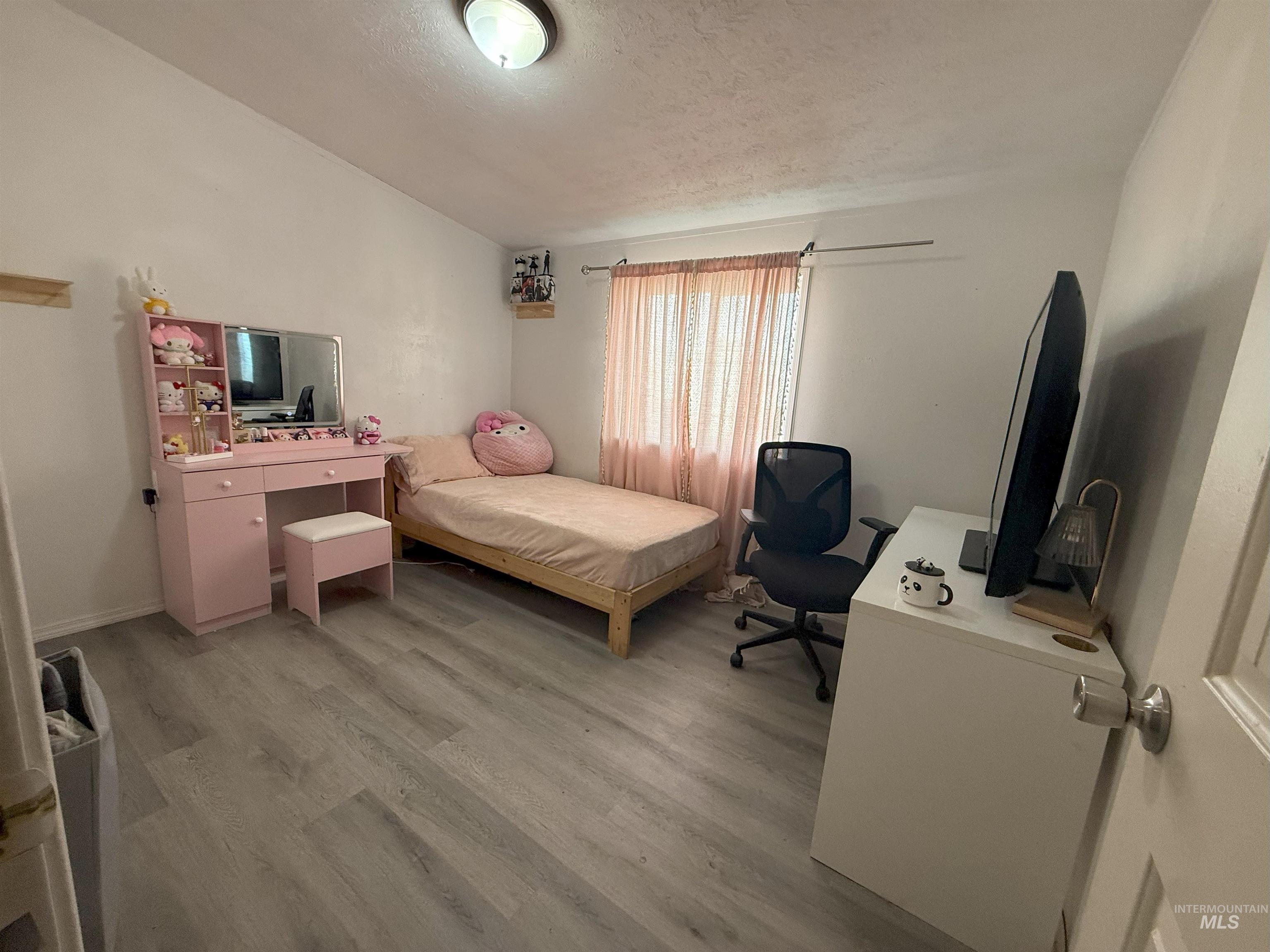 Bedroom with an office area, light wood finished floors, and a textured ceiling