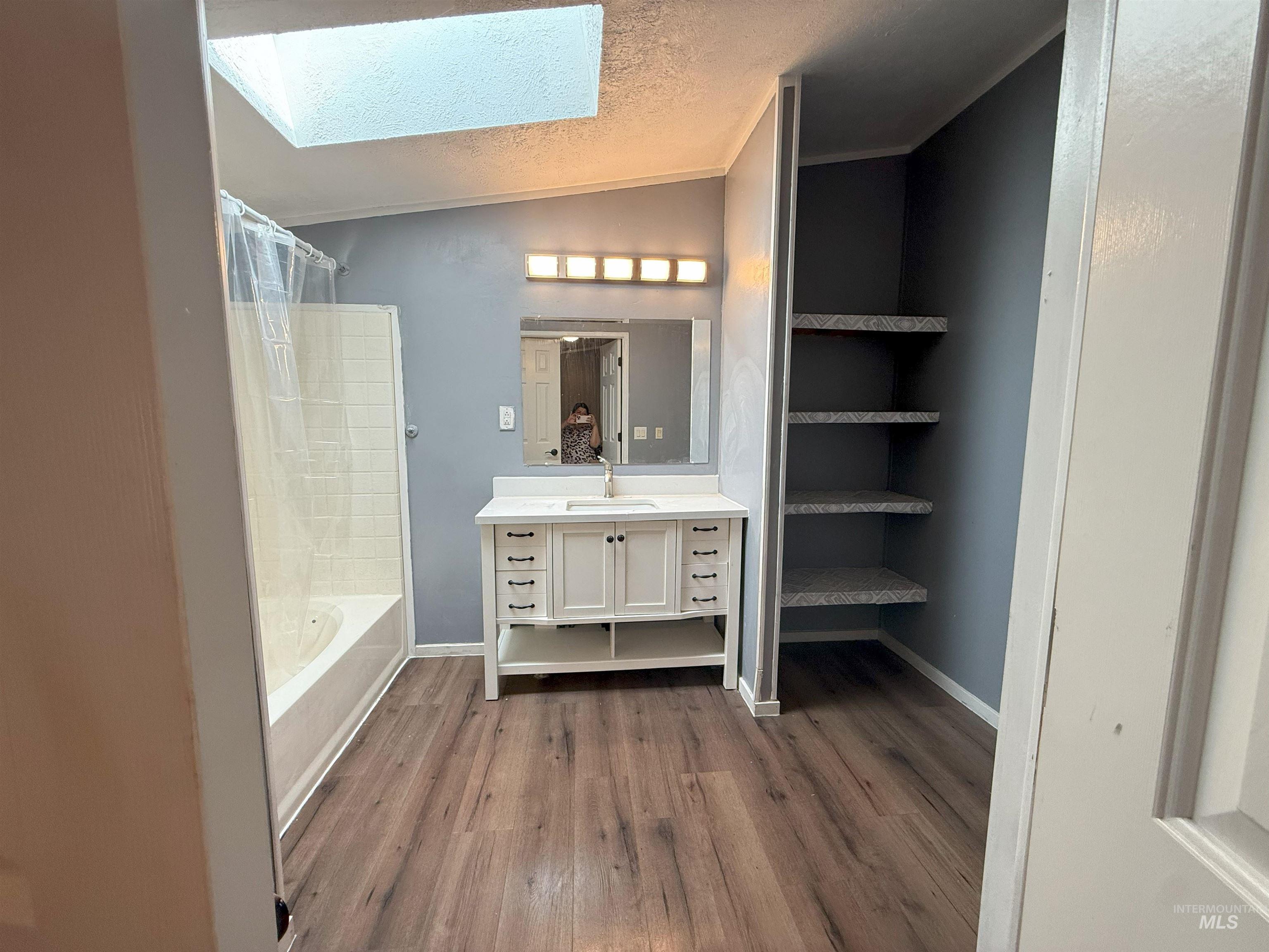 Bathroom featuring a textured ceiling, vanity, a skylight, dark wood-style flooring, and shower / bath combo with shower curtain