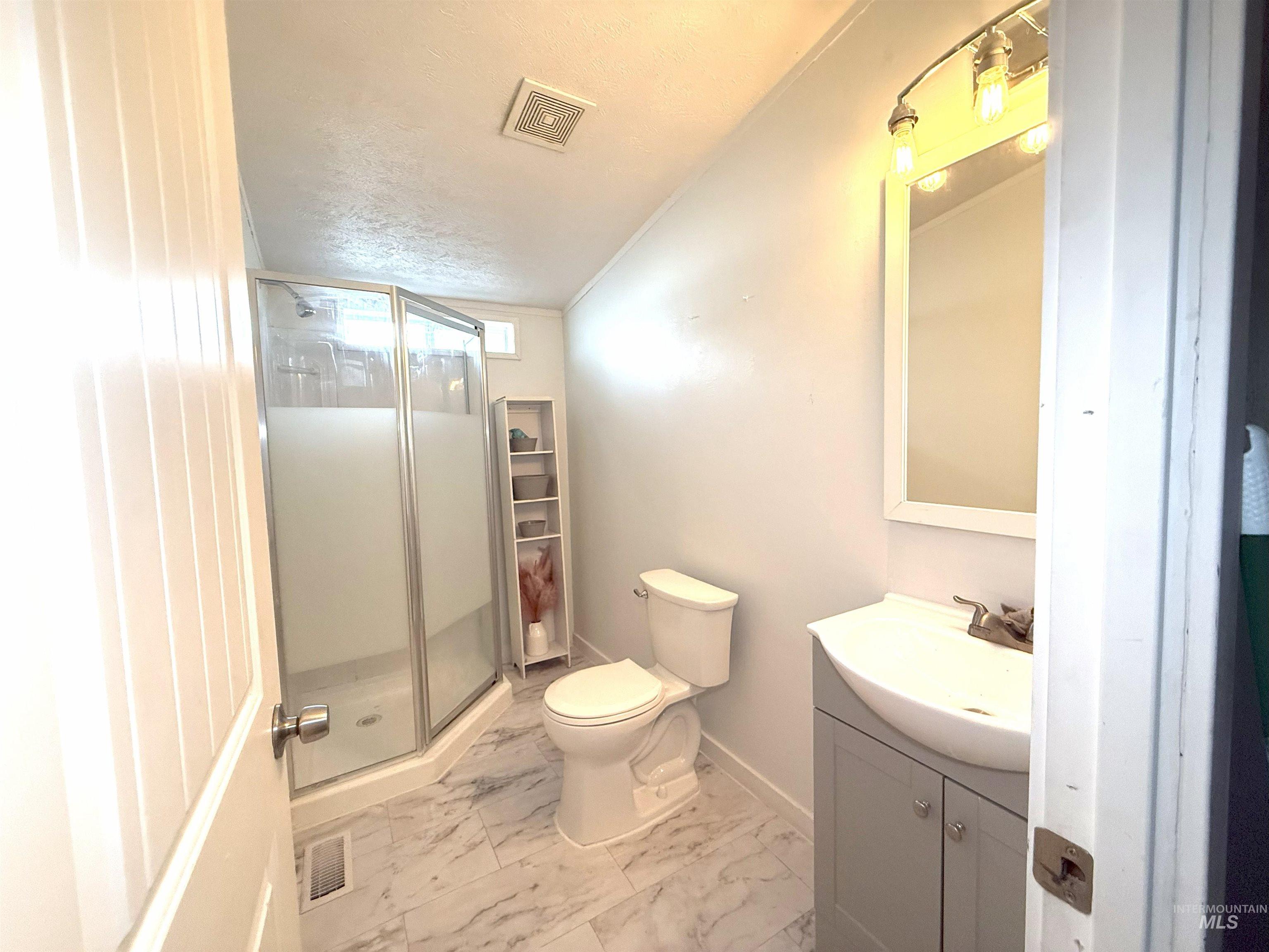 Bathroom featuring ornamental molding, vanity, a shower stall, a textured ceiling, and light marble finish flooring