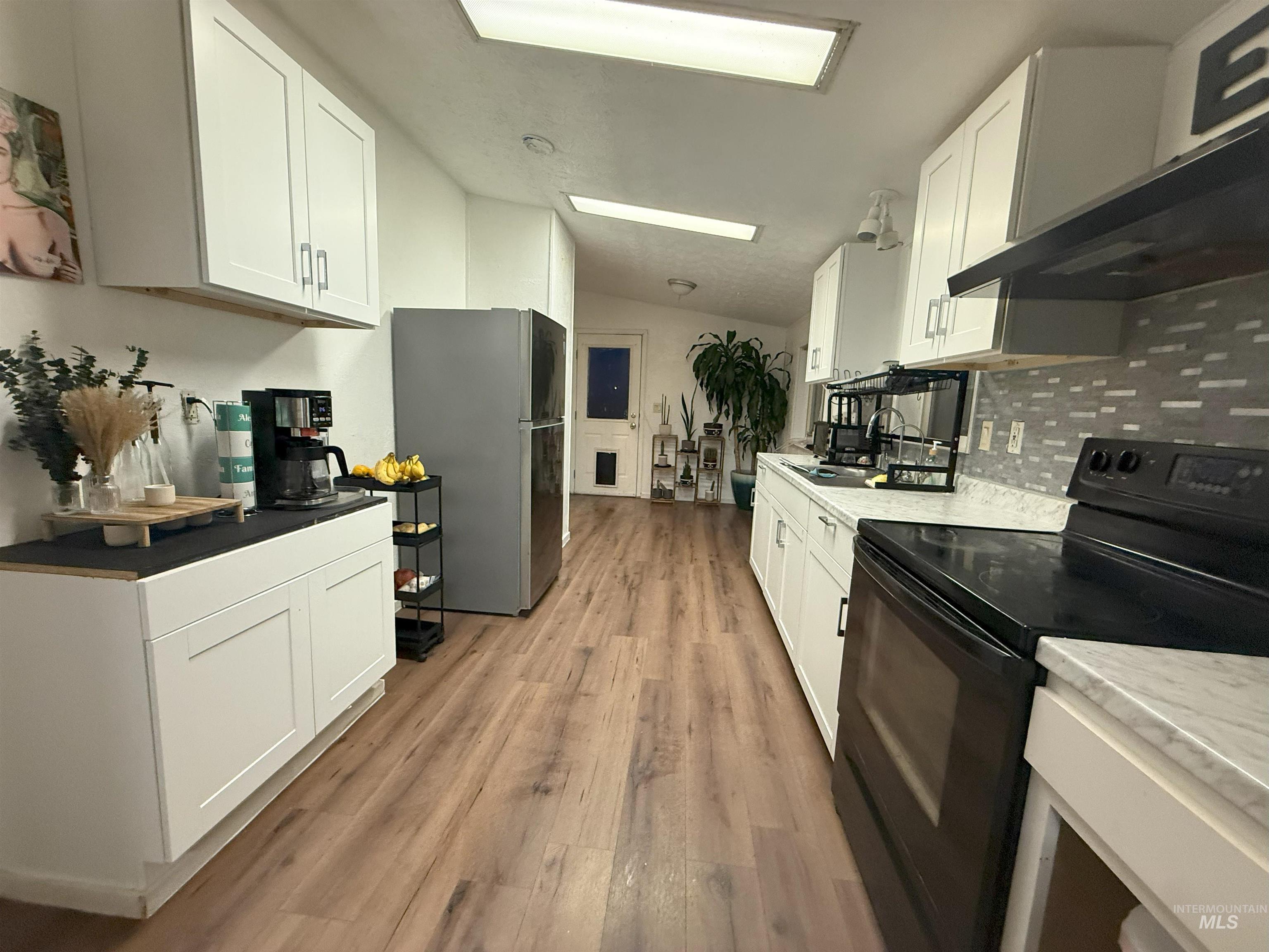 Kitchen with black electric range oven, vaulted ceiling, white cabinetry, freestanding refrigerator, and backsplash