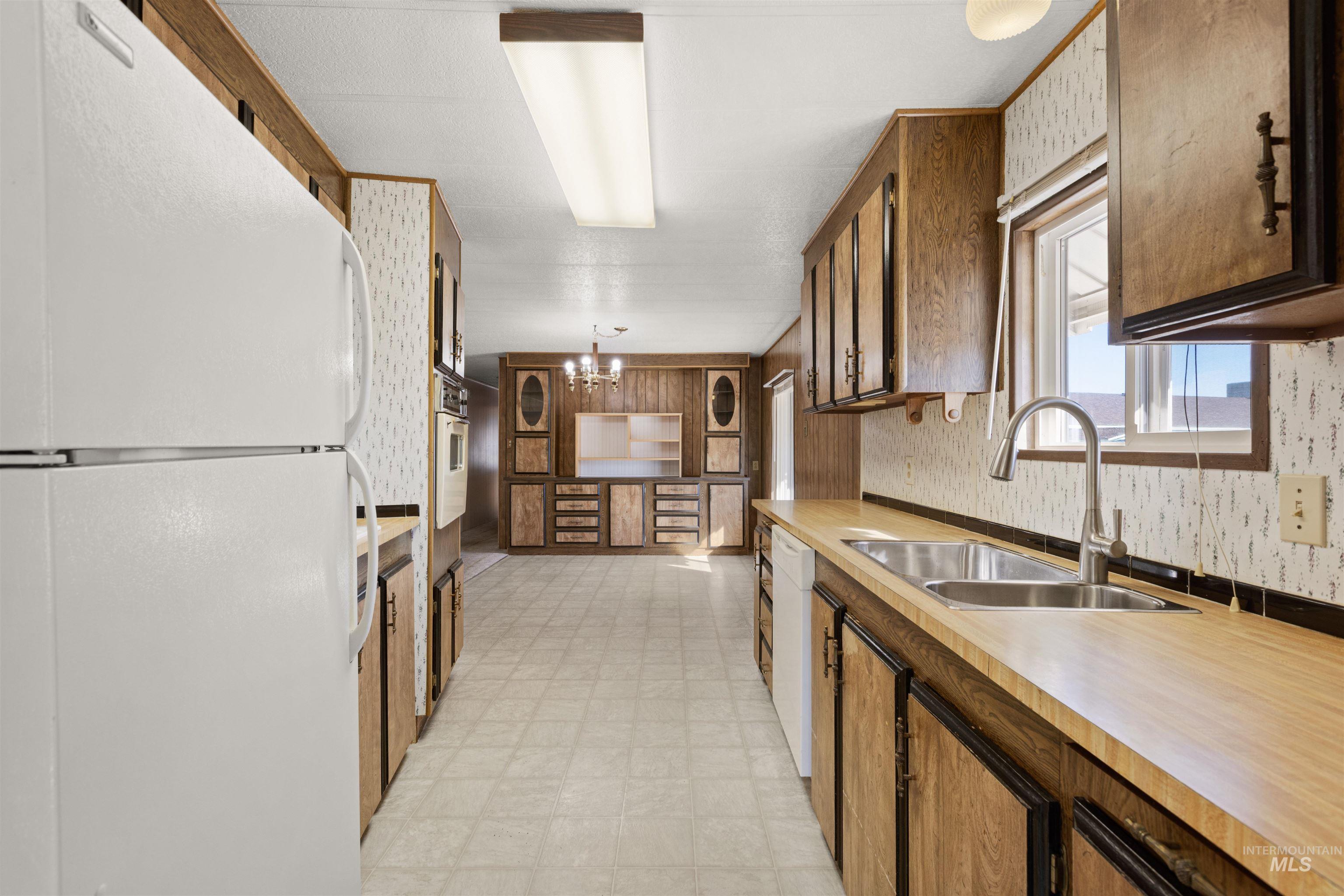 Kitchen featuring white appliances, light flooring, light countertops, wallpapered walls, and a chandelier
