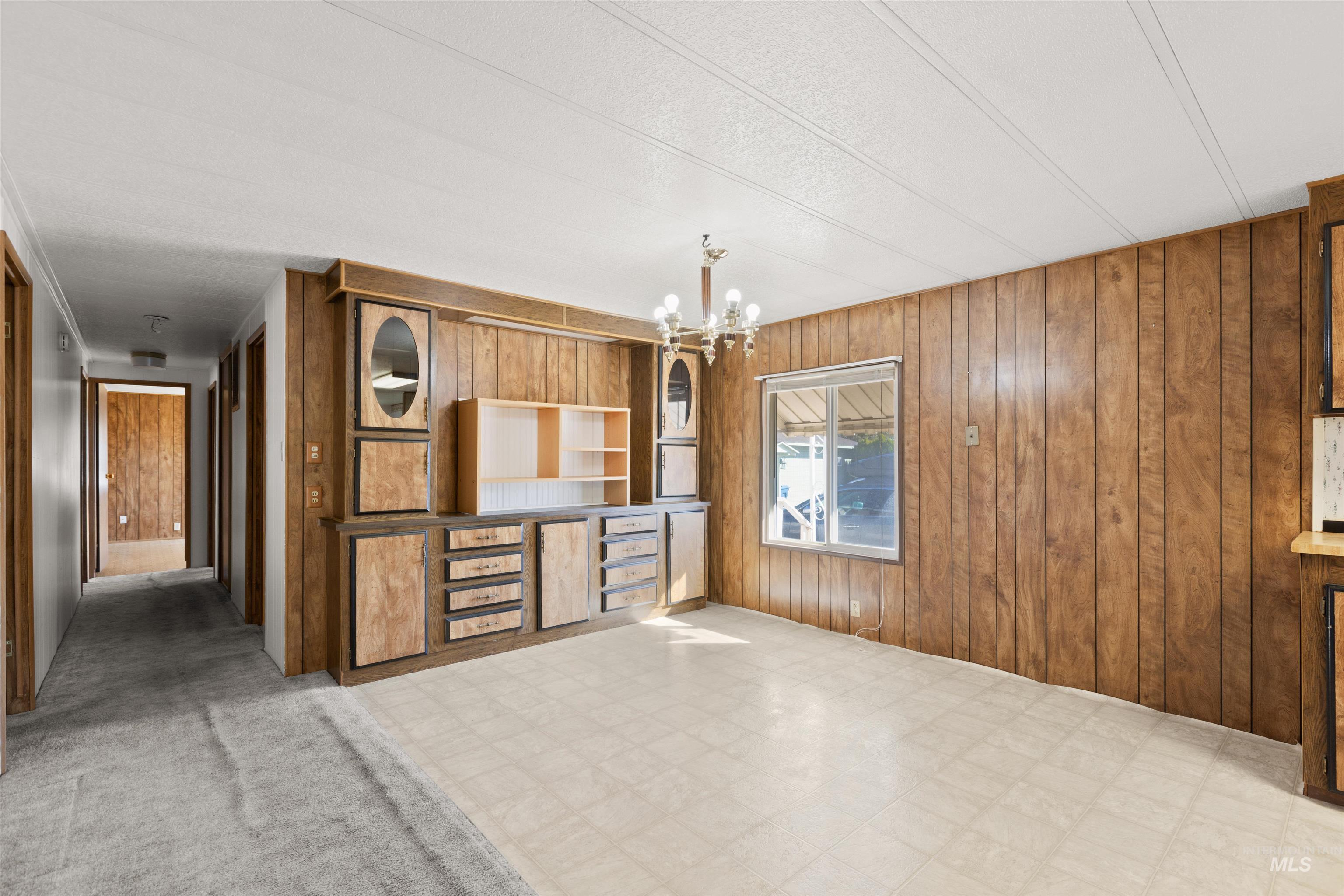 Dining Room featuring light floors, wood walls, a chandelier, and a textured ceiling